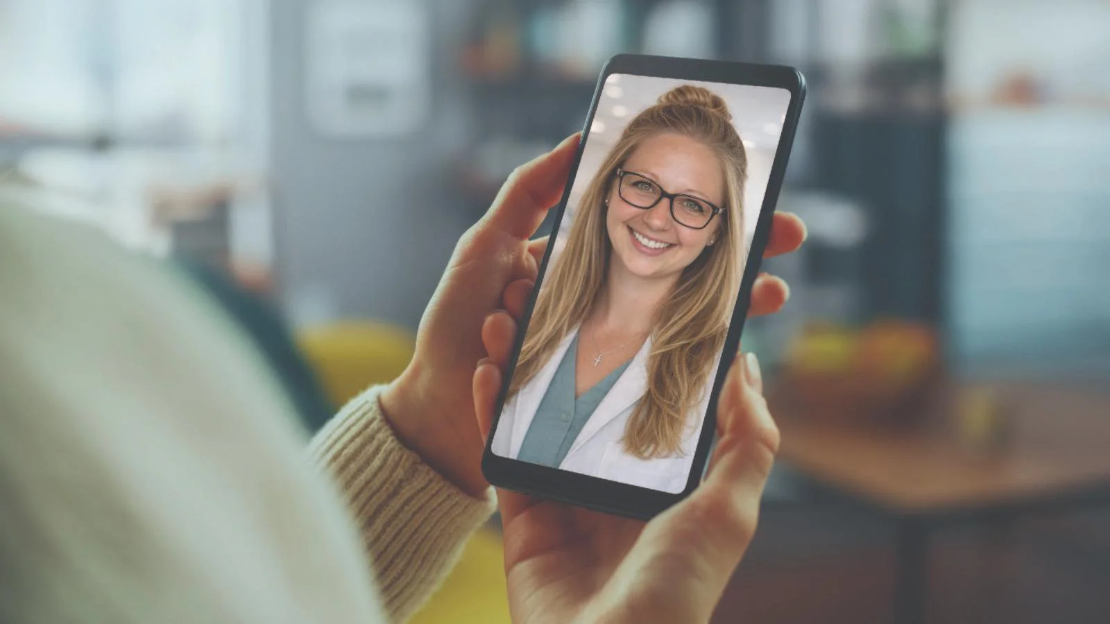Person holding a smartphone with a video call showing a smiling woman with glasses and long blonde hair.