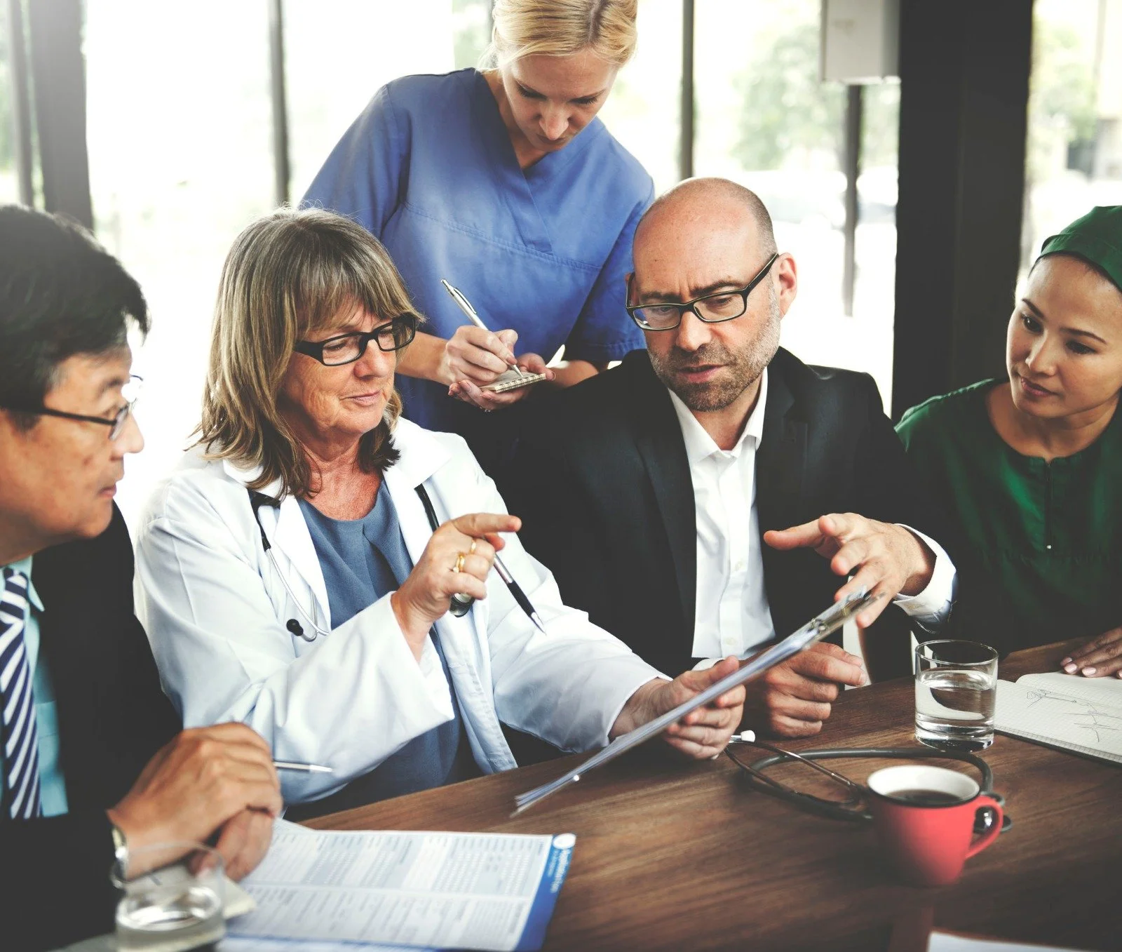 A group of healthcare professionals, including doctors and nurses, engaged in a discussion around a table in a conference room.