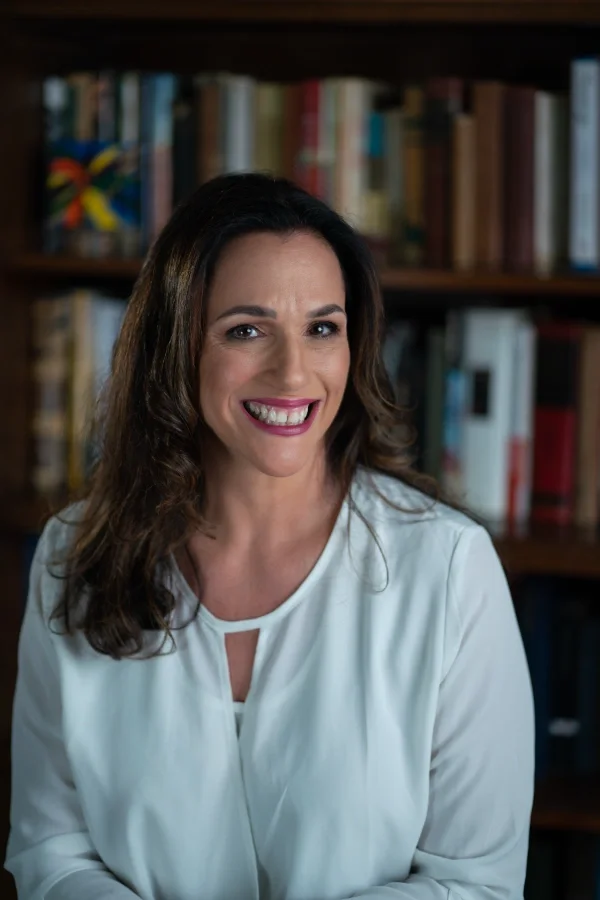 Lilah Brand, smiling, sitting in front of a bookshelf filled with books.