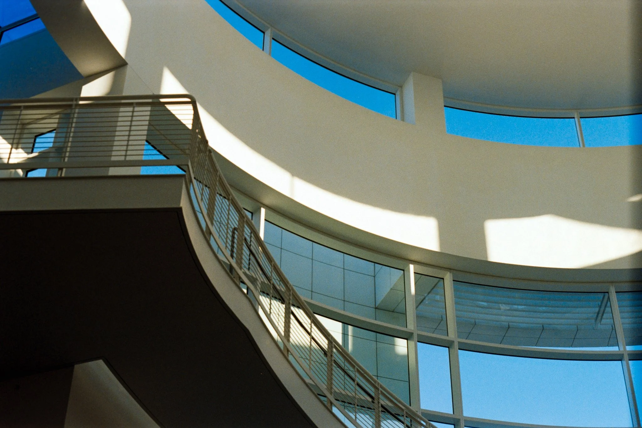 Interior view of a modern building with curved balconies, large windows, and a blue sky visible through the windows.