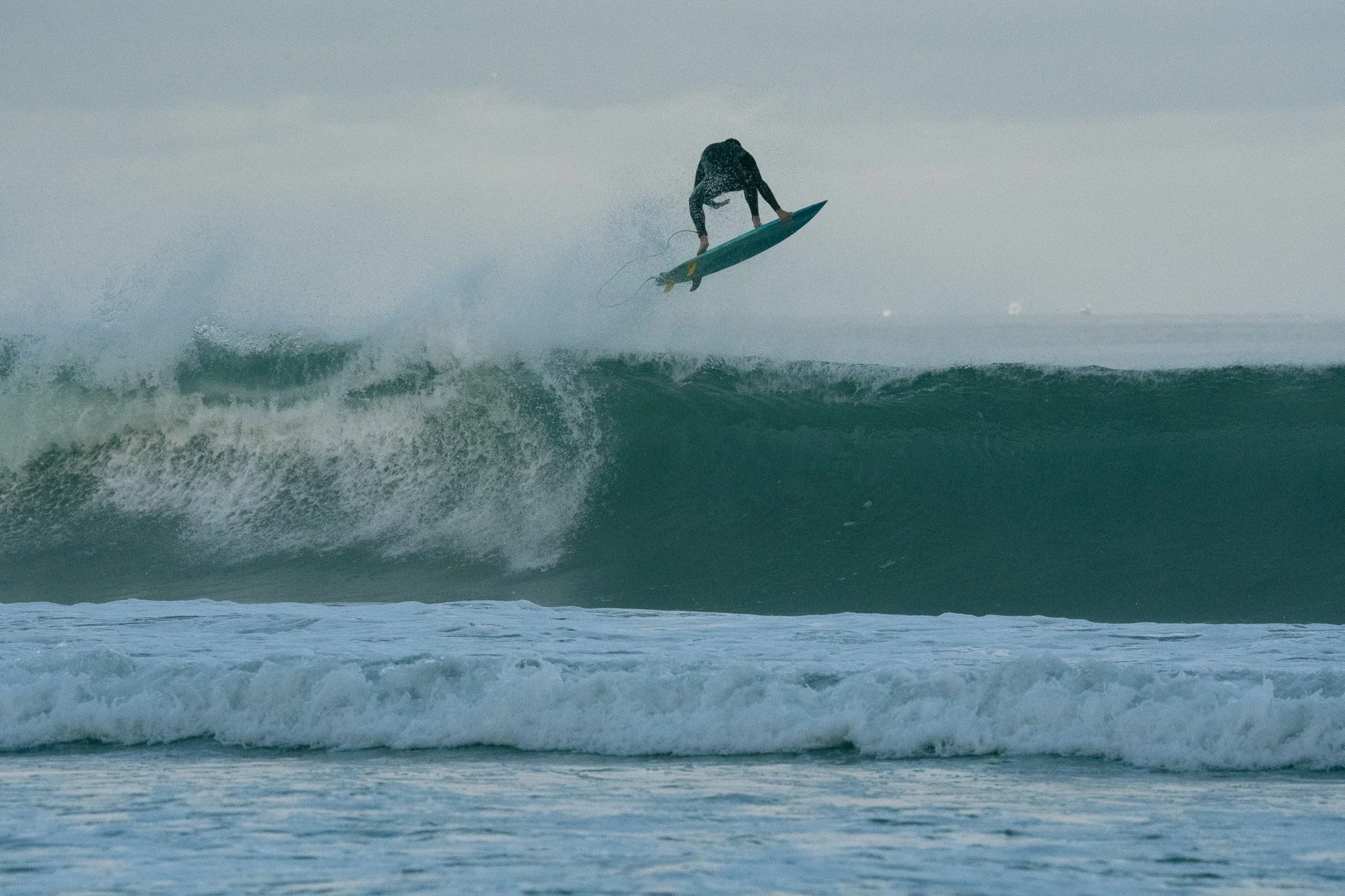 Surfer in a wetsuit performing a mid-air trick on a surfboard over ocean waves.