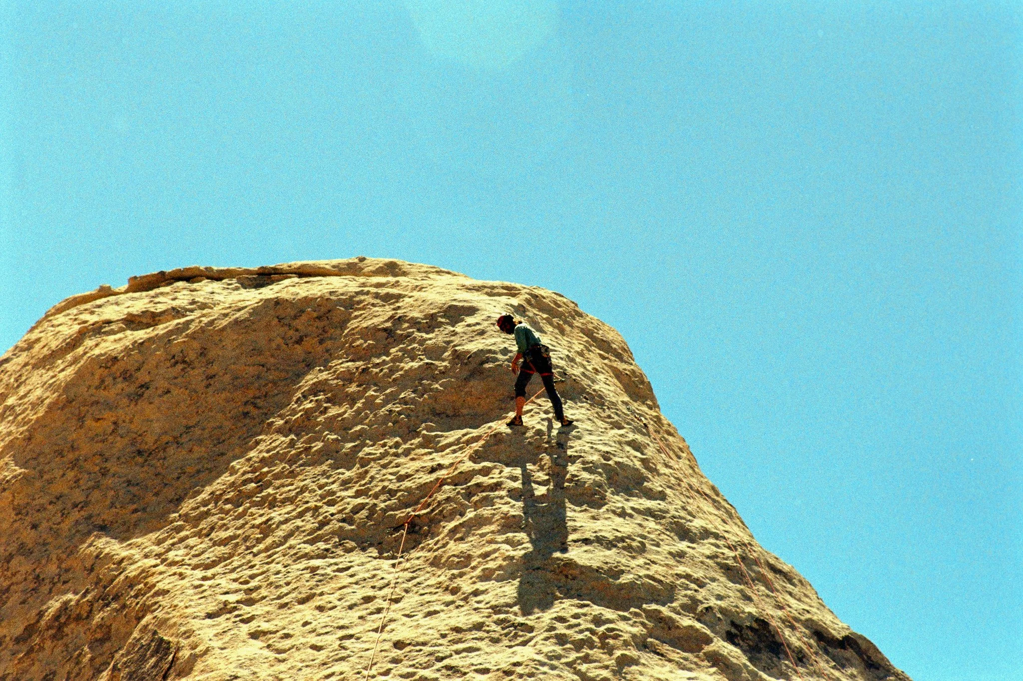 A person rappelling down a large rock formation against a clear blue sky.