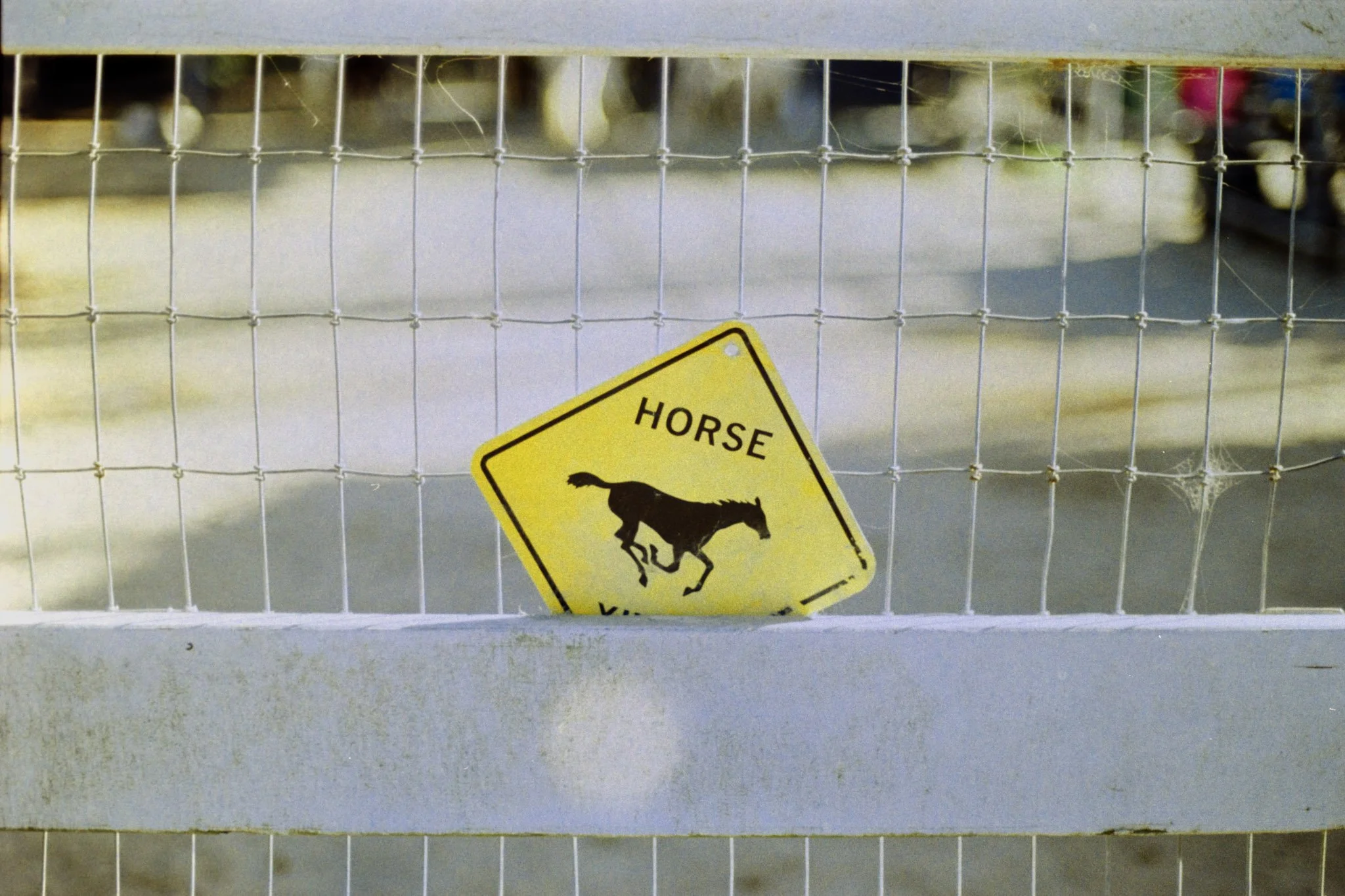 A wire fence with a yellow warning sign showing a horse, partially obscured at the bottom, behind the fence.