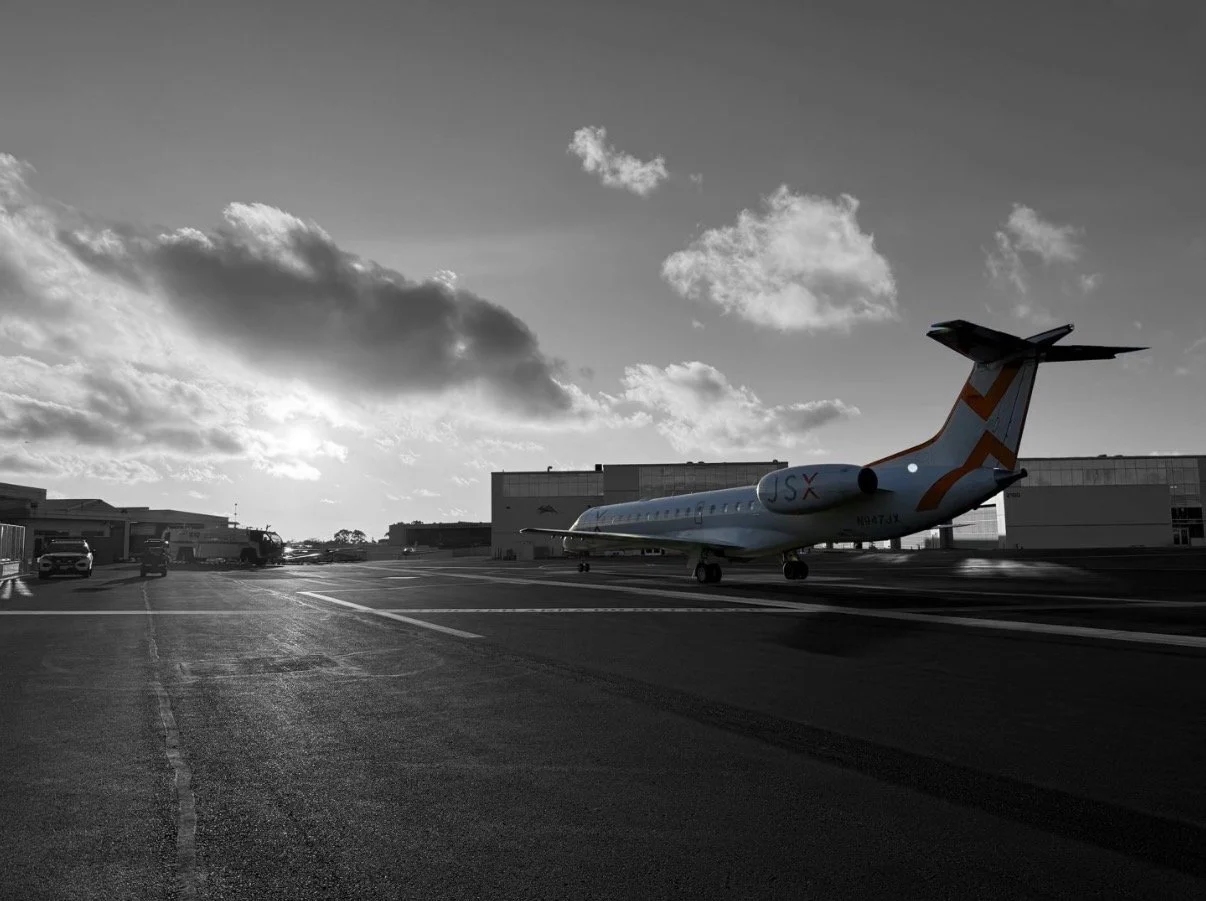 An airplane on the tarmac of an airport during sunset or sunrise with clouds in the sky and a few vehicles around.