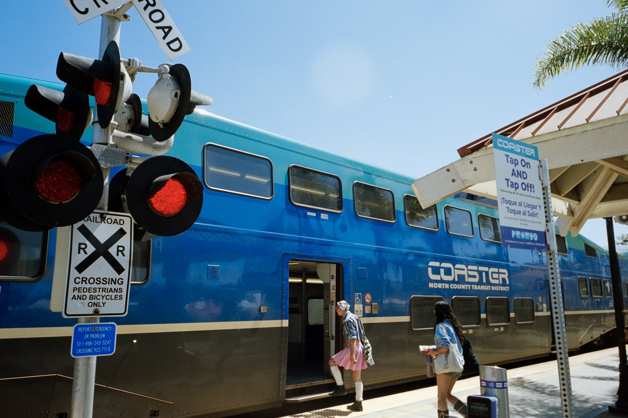 Blue train car at a station with people boarding, a sign for the coaster ride, and a traffic light with red signals.