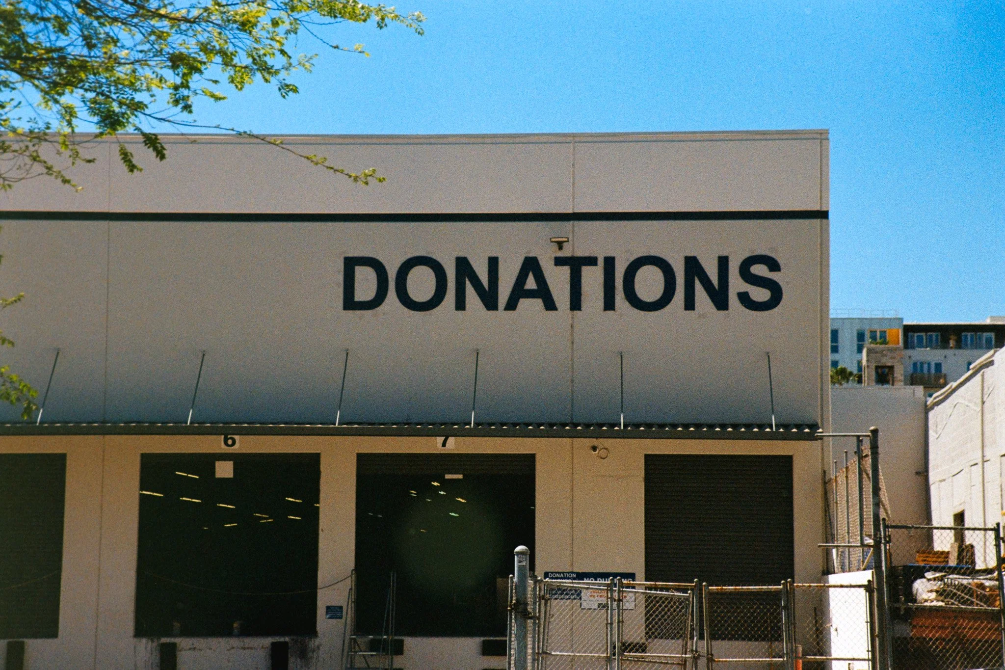 A large building with a sign that reads 'DONATIONS' on its front. The building appears to be a parking structure with an open entrance, behind which part of the interior can be seen. There are trees and a clear blue sky above.
