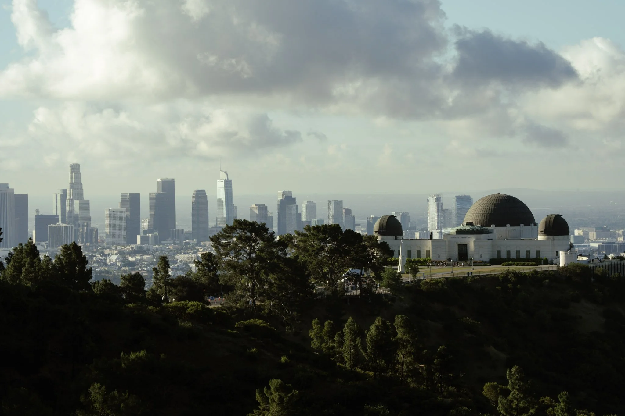City skyline with tall skyscrapers and a planetarium building in the foreground, under a cloudy sky.