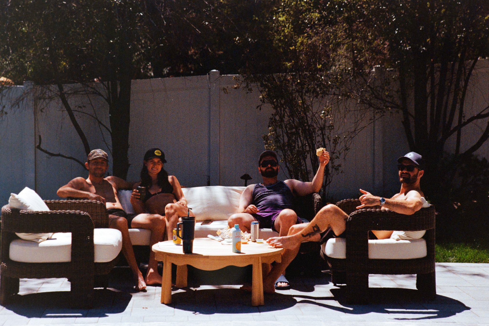 Four people are sitting on outdoor furniture around a coffee table at night. They are smiling and appear to be relaxing and enjoying each other's company.