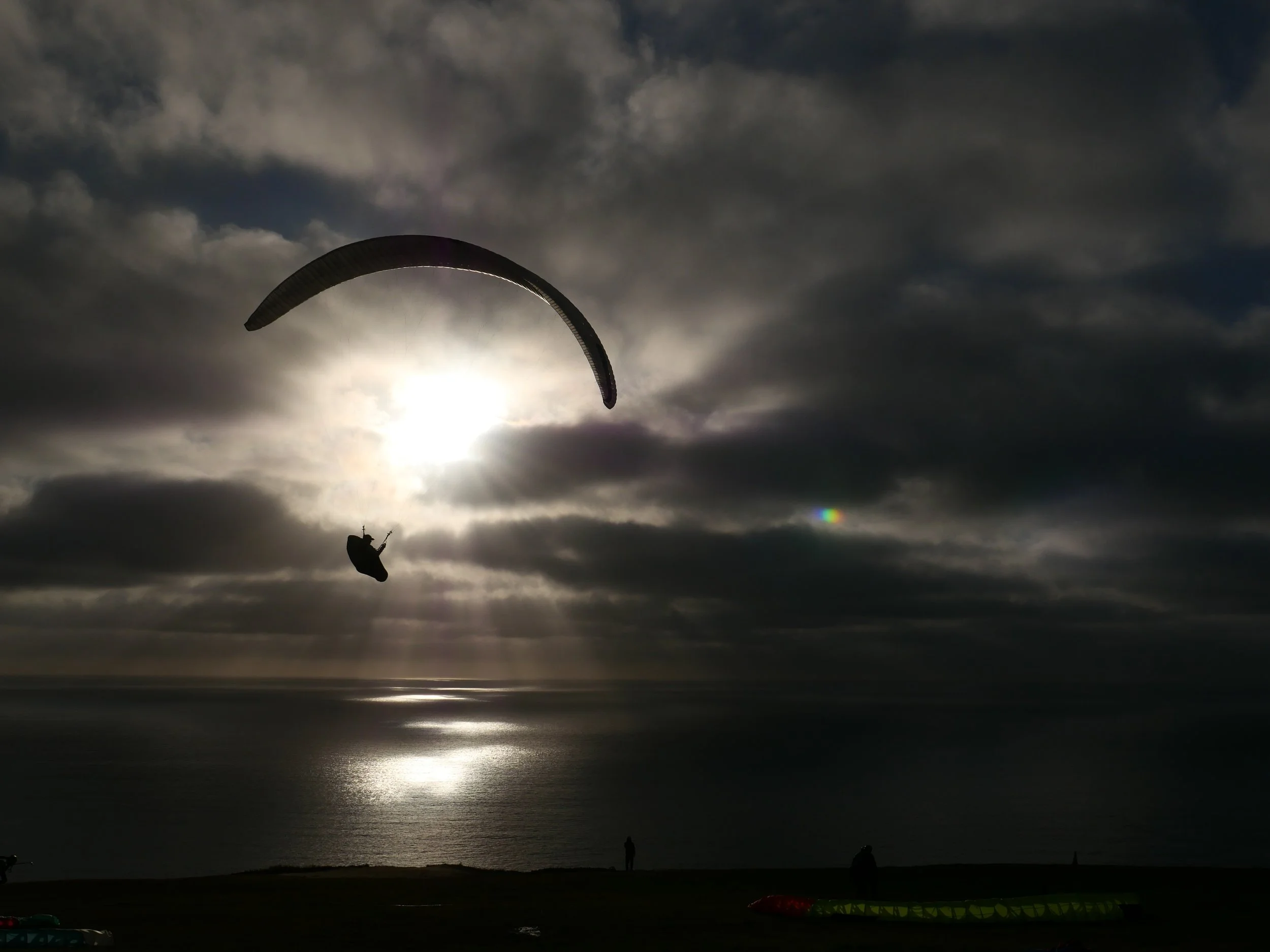 Kite surfer in the air over the ocean with dramatic cloudy sky and sunlight breaking through.