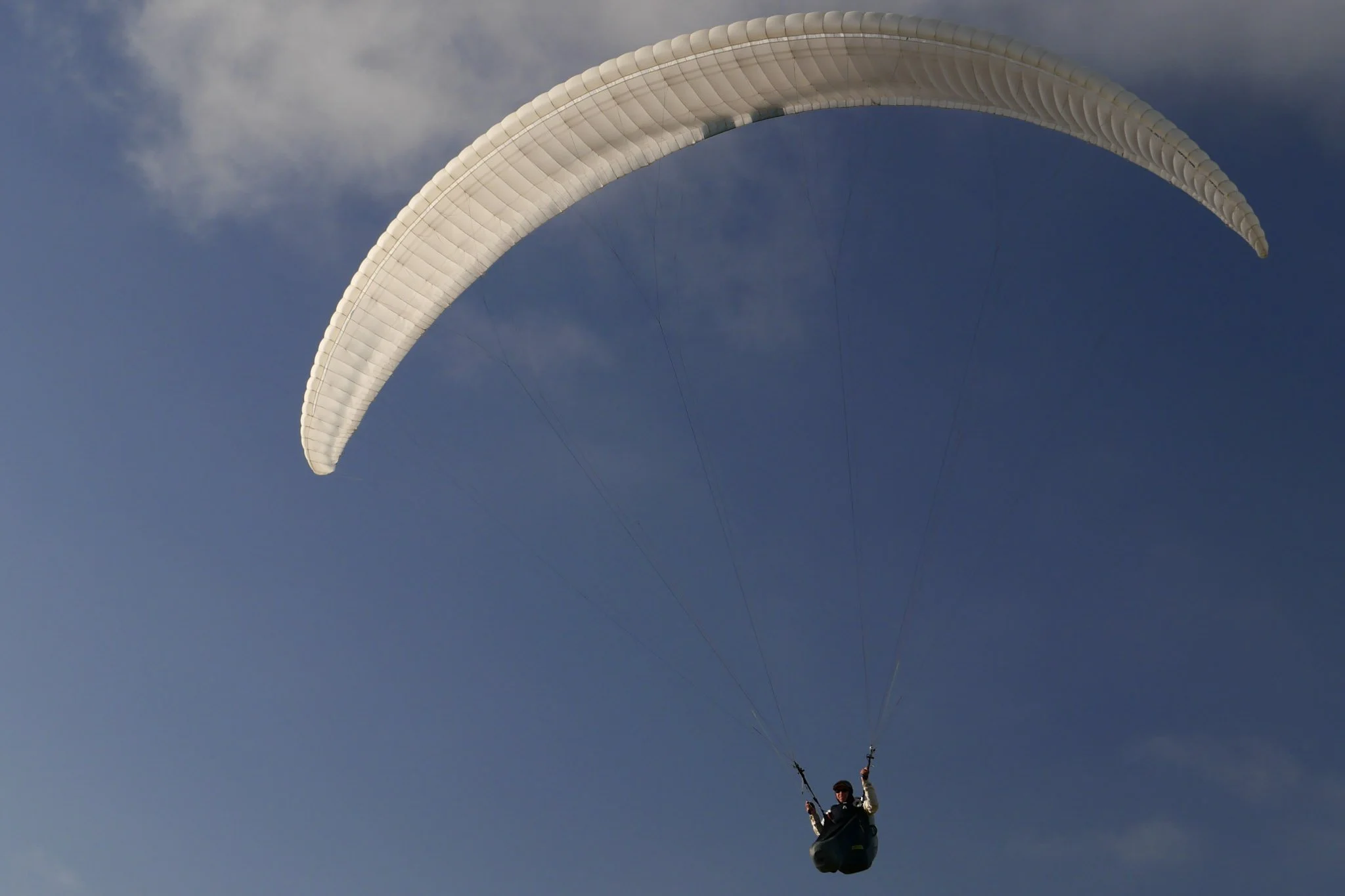 A person paragliding in the sky with a white parachute amidst some clouds.