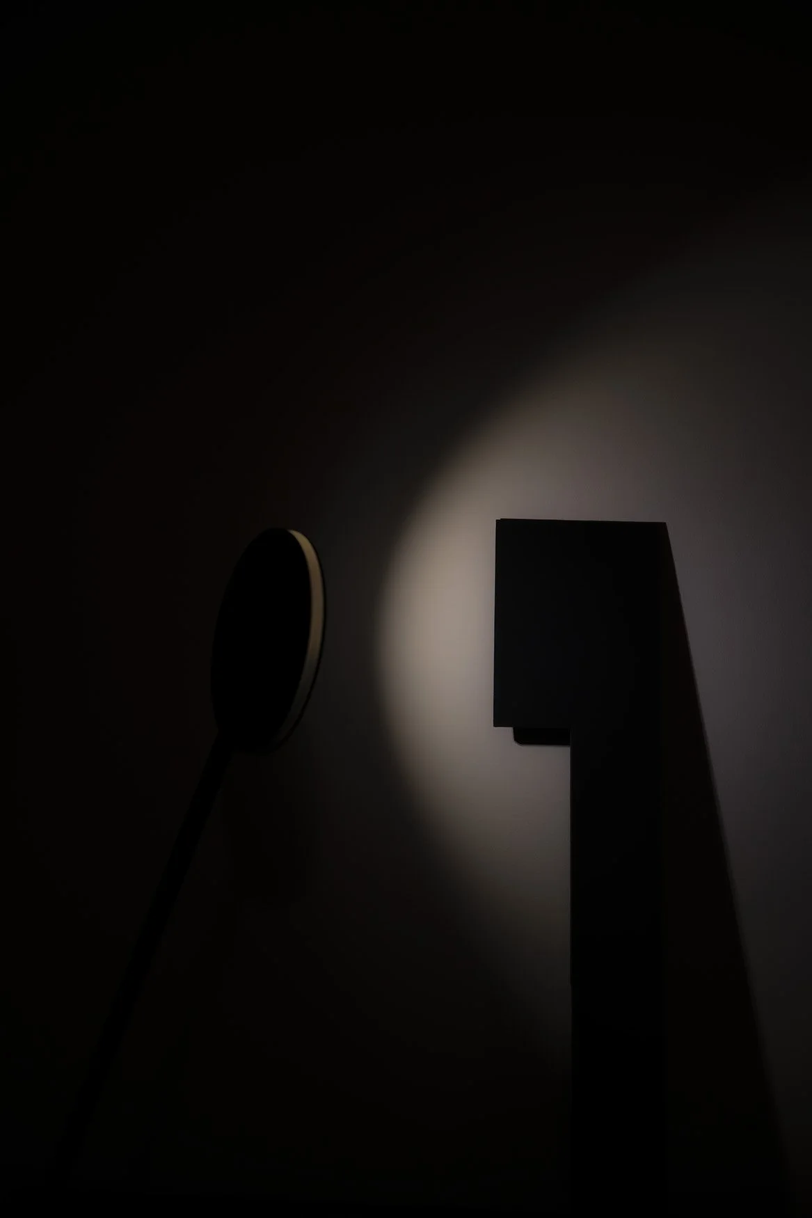 Silhouette of a geometric sculpture illuminated by a focused light in a dark room.