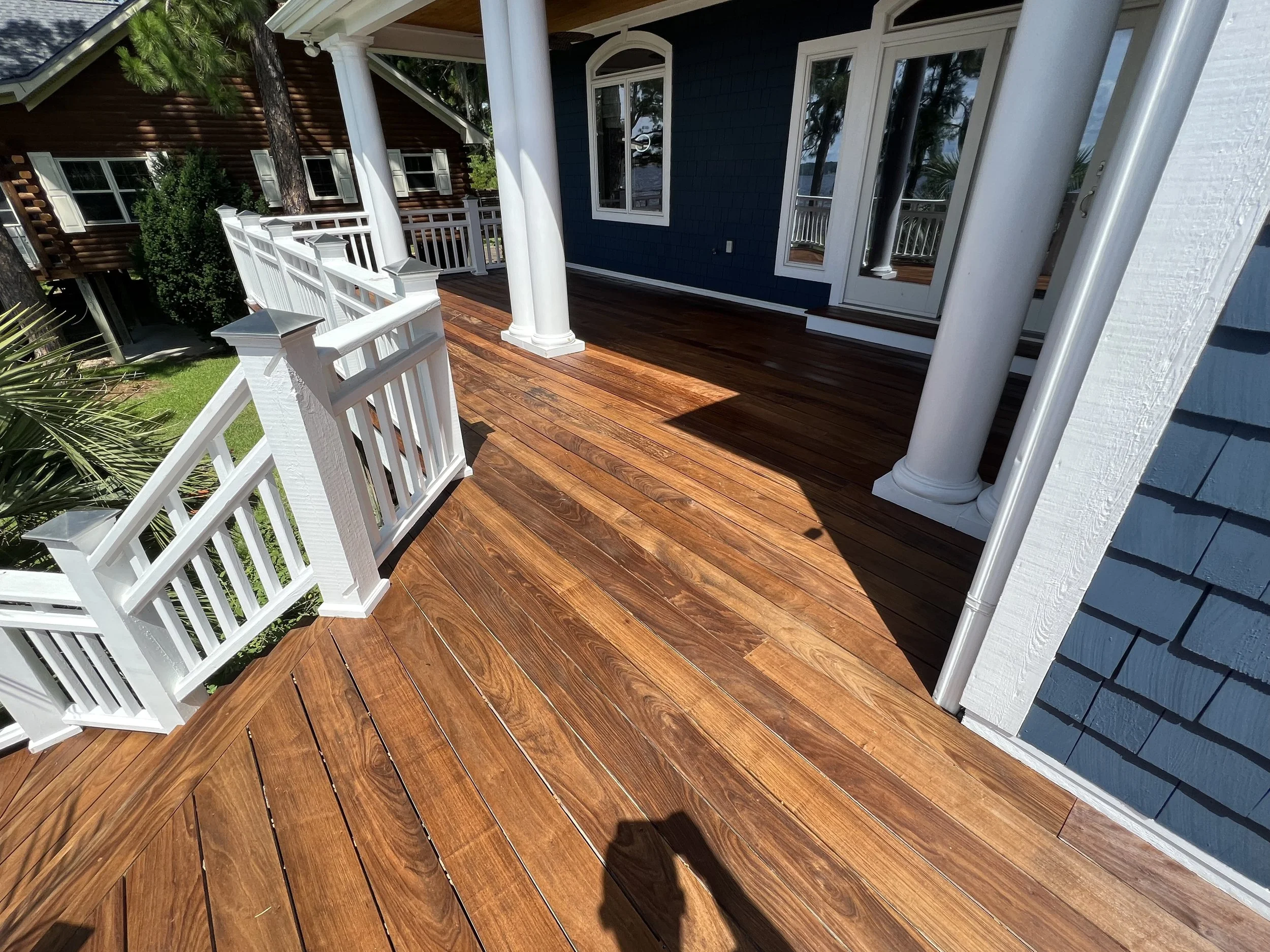 Photo of a wooden deck outside a house with blue and brown siding, white railings, and four white columns.