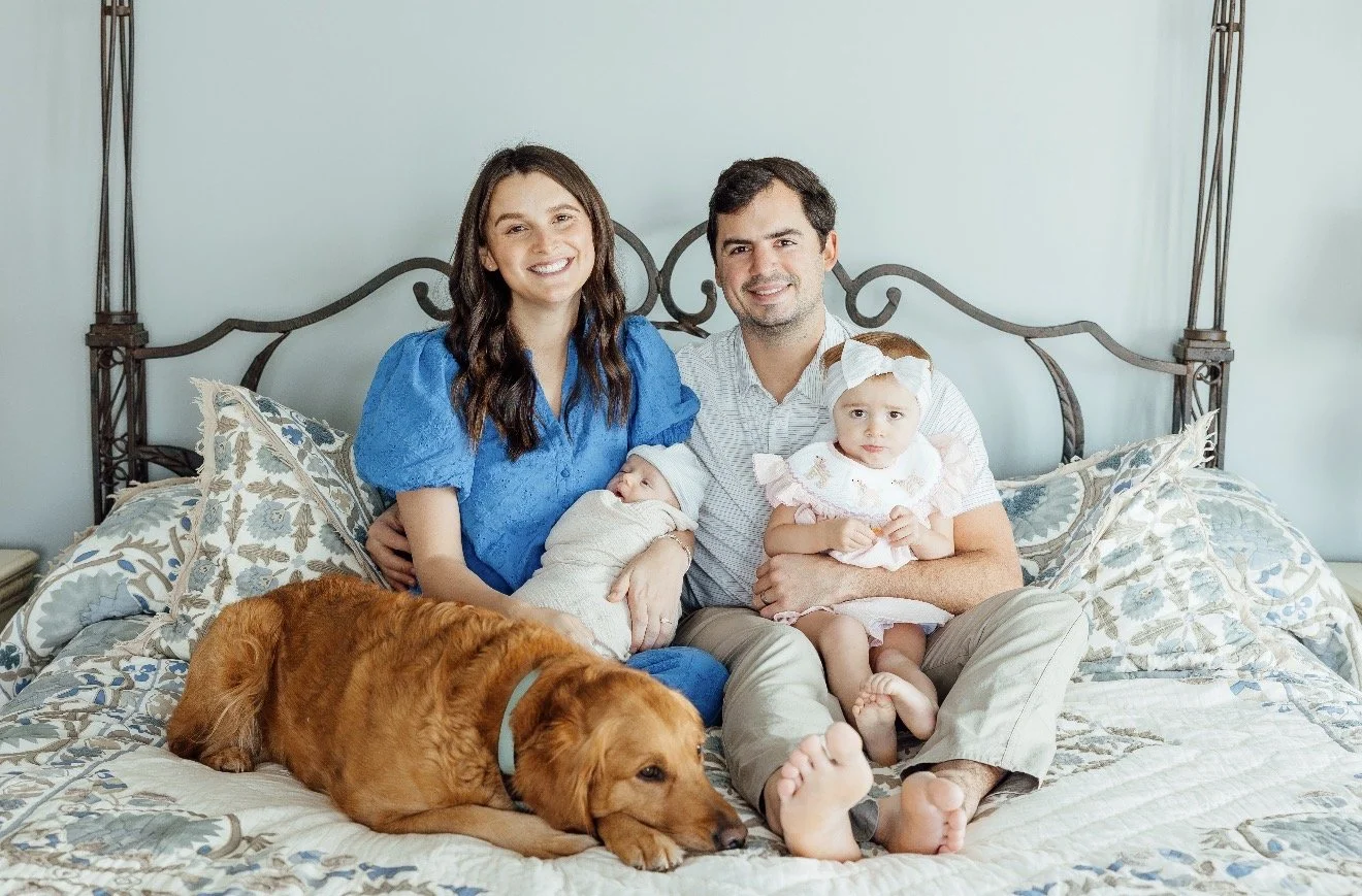 Family with two children and a dog sitting on a bed in a bedroom.