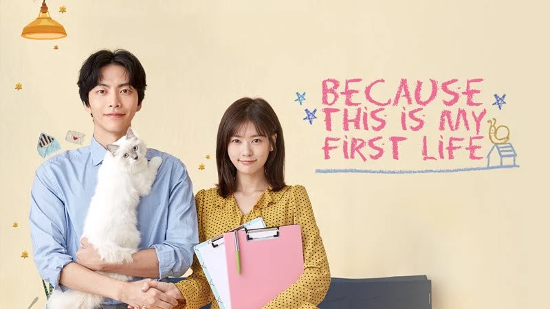 Two characters from the Korean drama Because This Is My First Life sitting together with a cat.