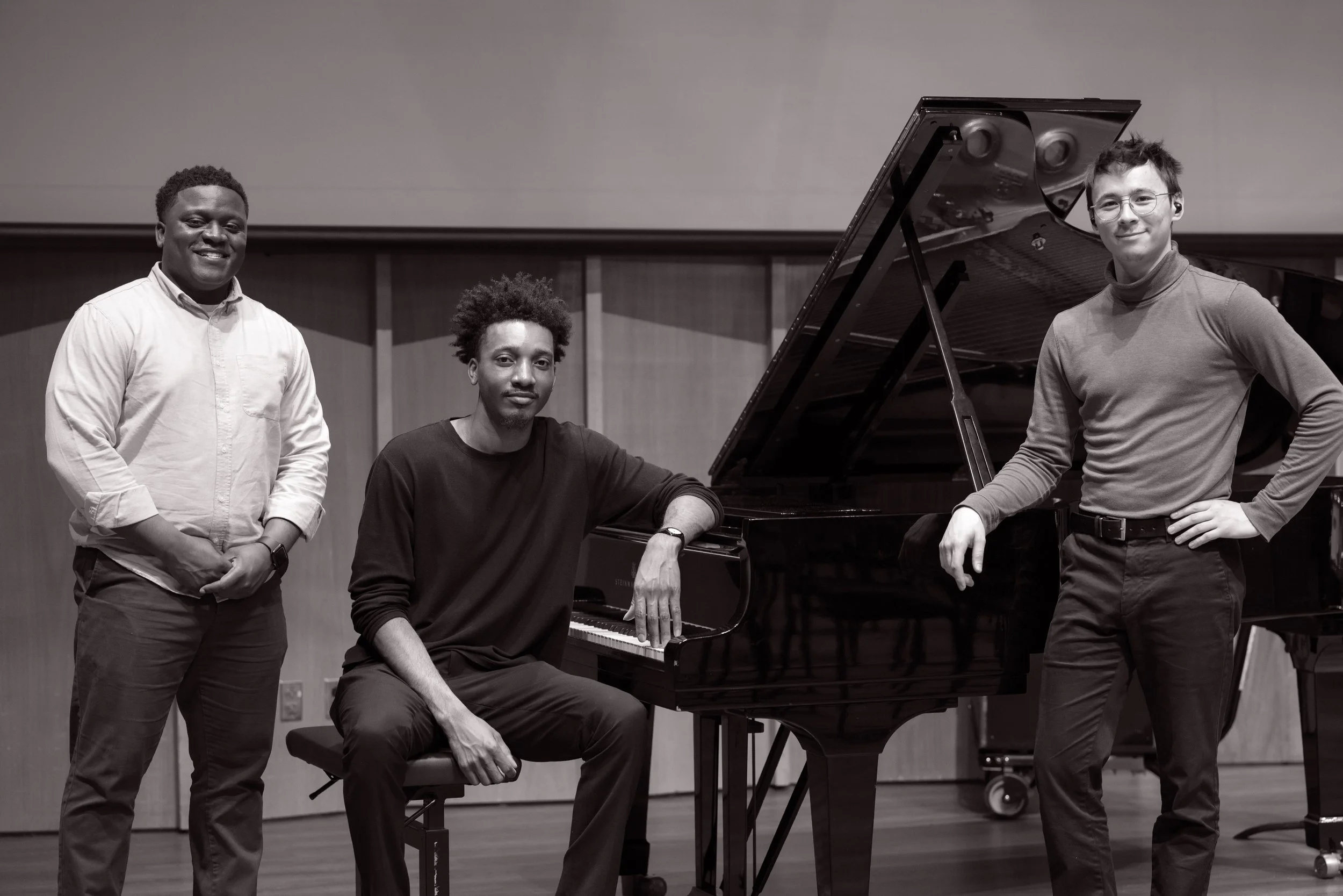 Isaiah Jones Jr. , Sid Smith IV, and Nat Lin near a grand piano in a music room. One is sitting at the piano, one is standing to the left, and the third is standing to the right.