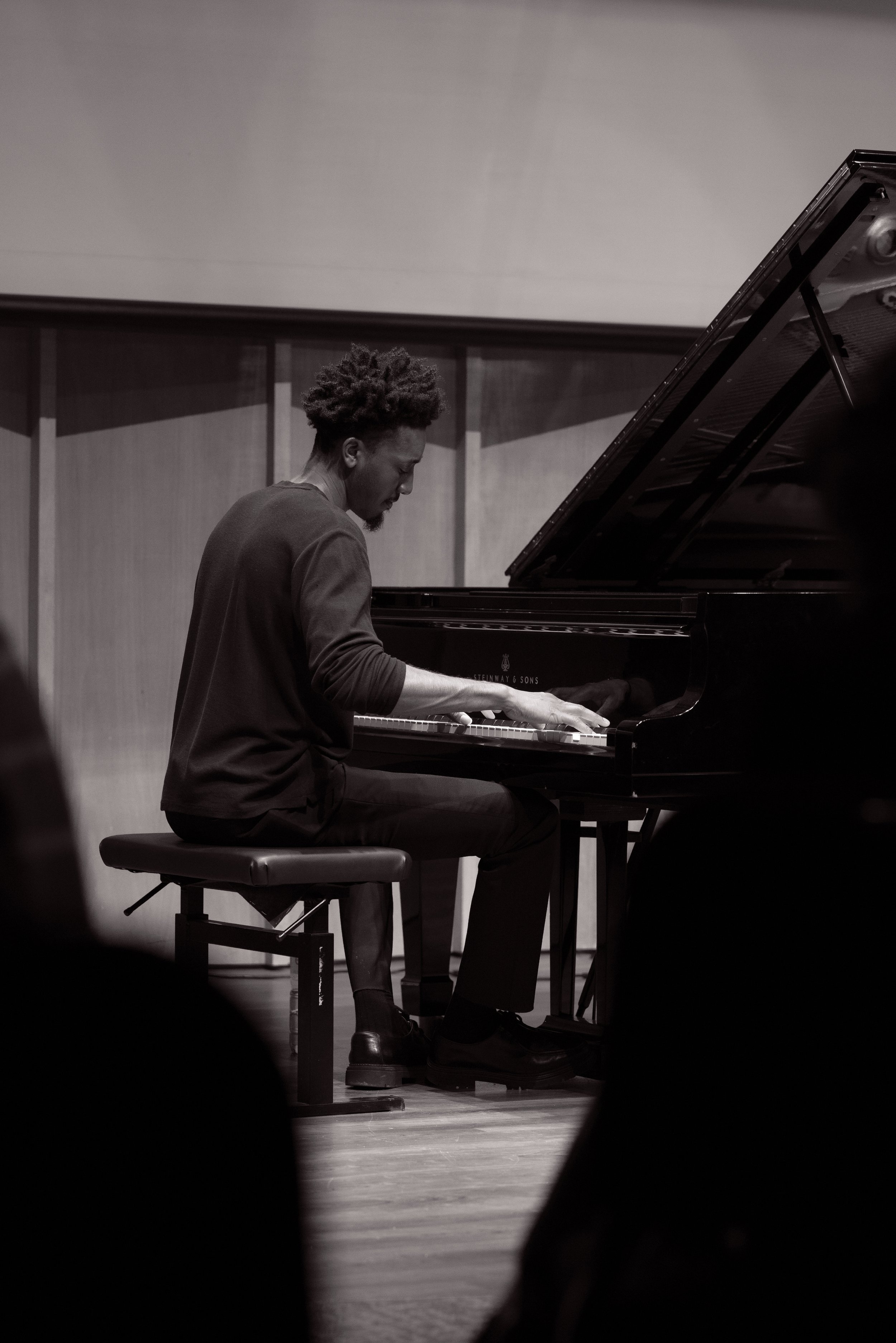 A musician playing a grand piano on stage, captured in black and white.