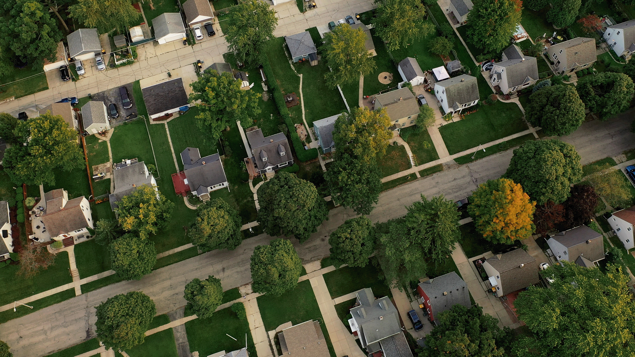 Aerial view of a neighborhood with houses, trees, yards, and streets.