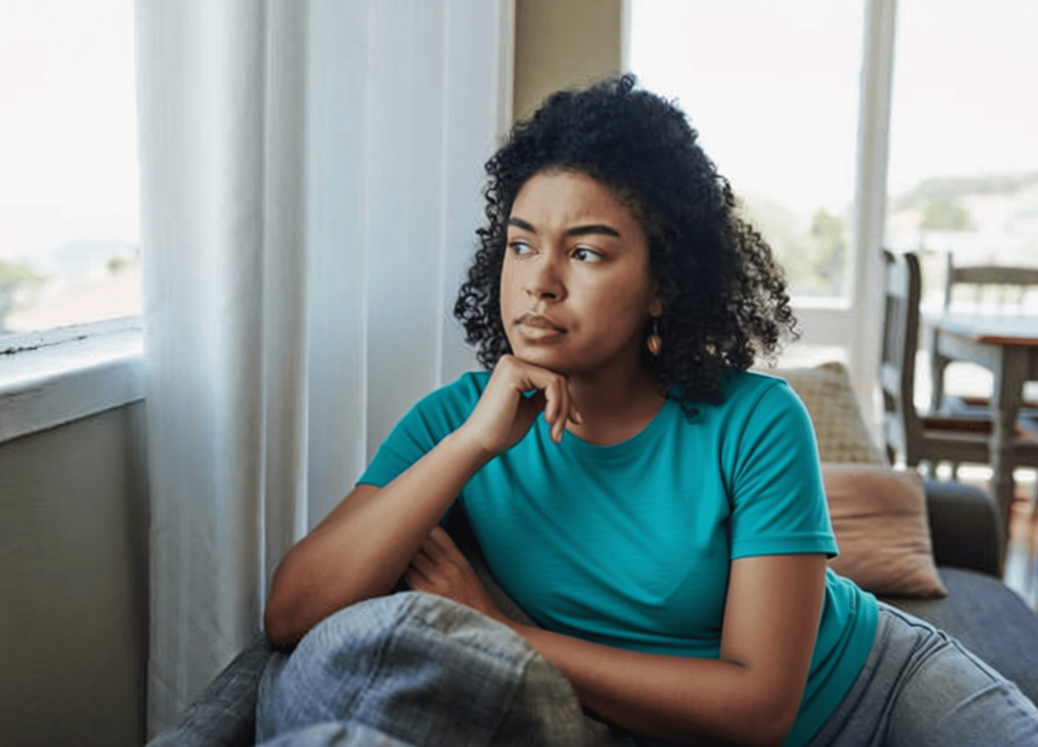 Young woman sitting on a couch looking out the window reflecting on anxiety and depression, representing therapy support for women at Throughline Psychotherapy in Raleigh, NC