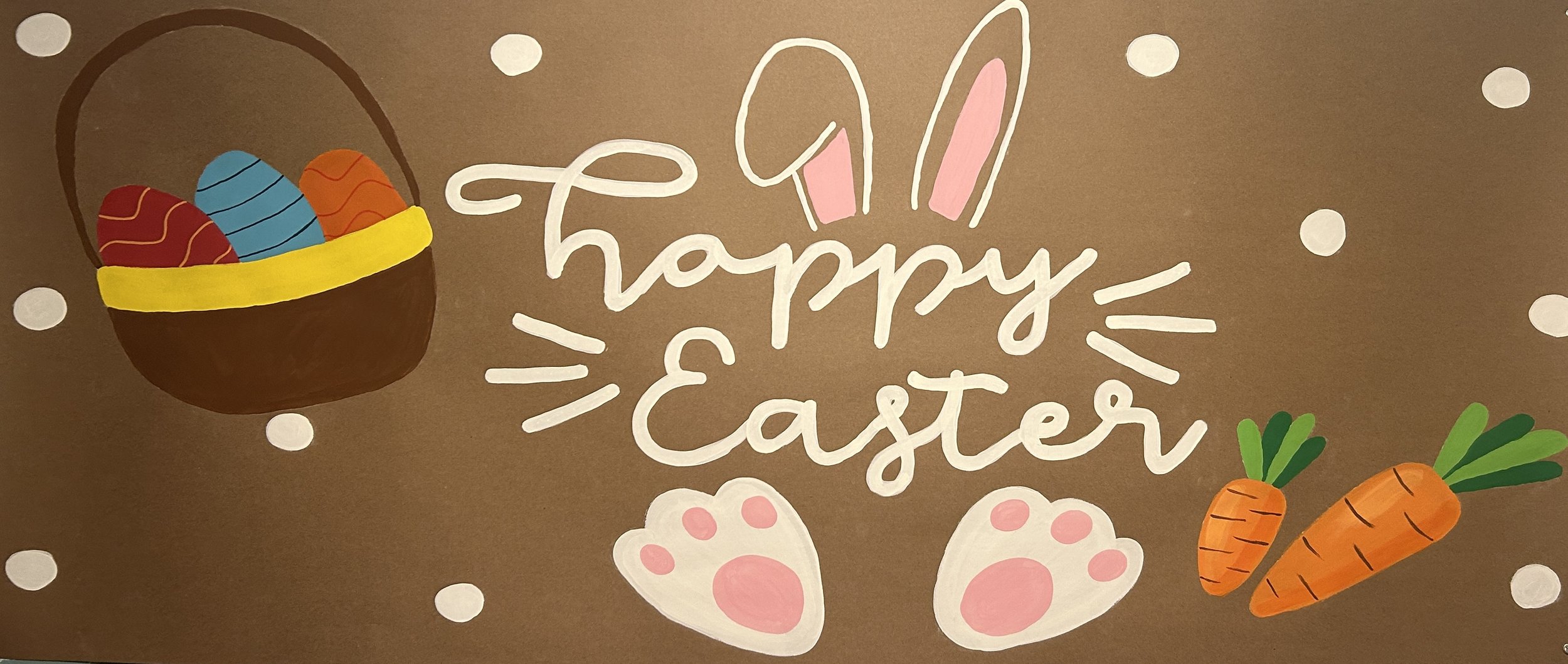 Easter greeting card with a brown background, illustrated with a basket of colorful decorated eggs, pink and white bunny ears, pink paw prints, and two orange carrots with green tops. The words "happy easter" are written in white in the center.