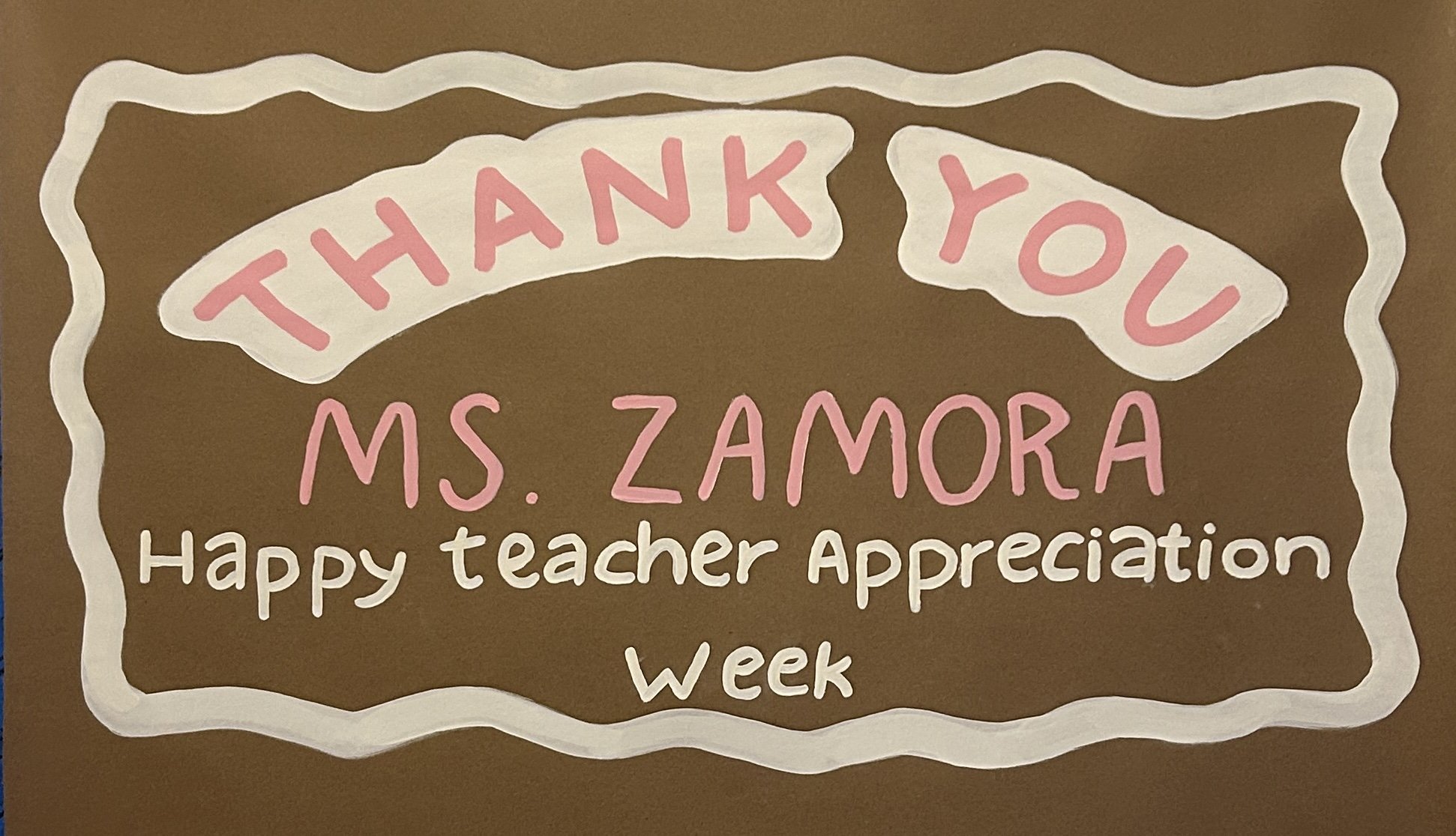 A handmade poster with a brown background, white wavy border, and pink and white text that reads, 'Thank You Ms. Zamora Happy Teacher Appreciation Week.'