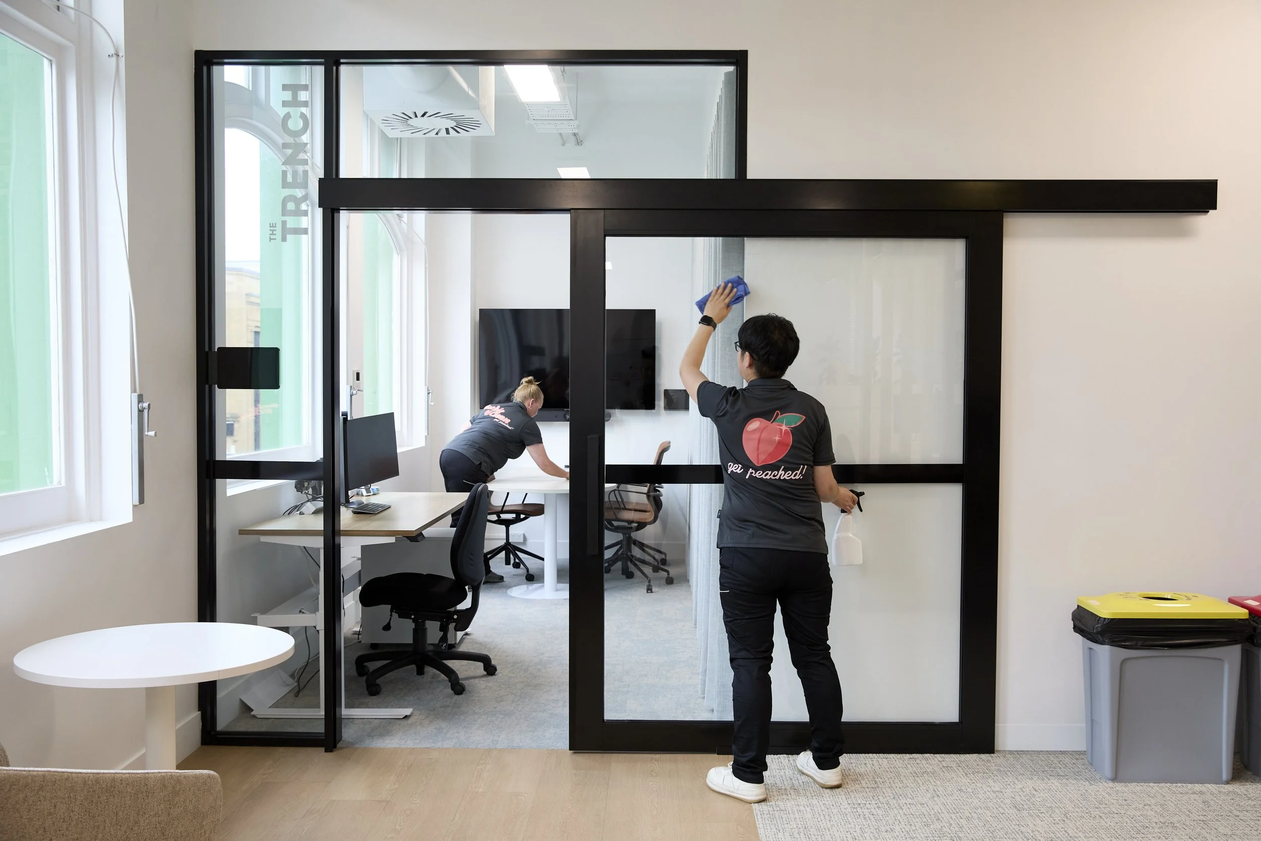 Peachie Clean team performing office cleaning in Hobart, wiping glass doors and desks in a modern commercial workspace
