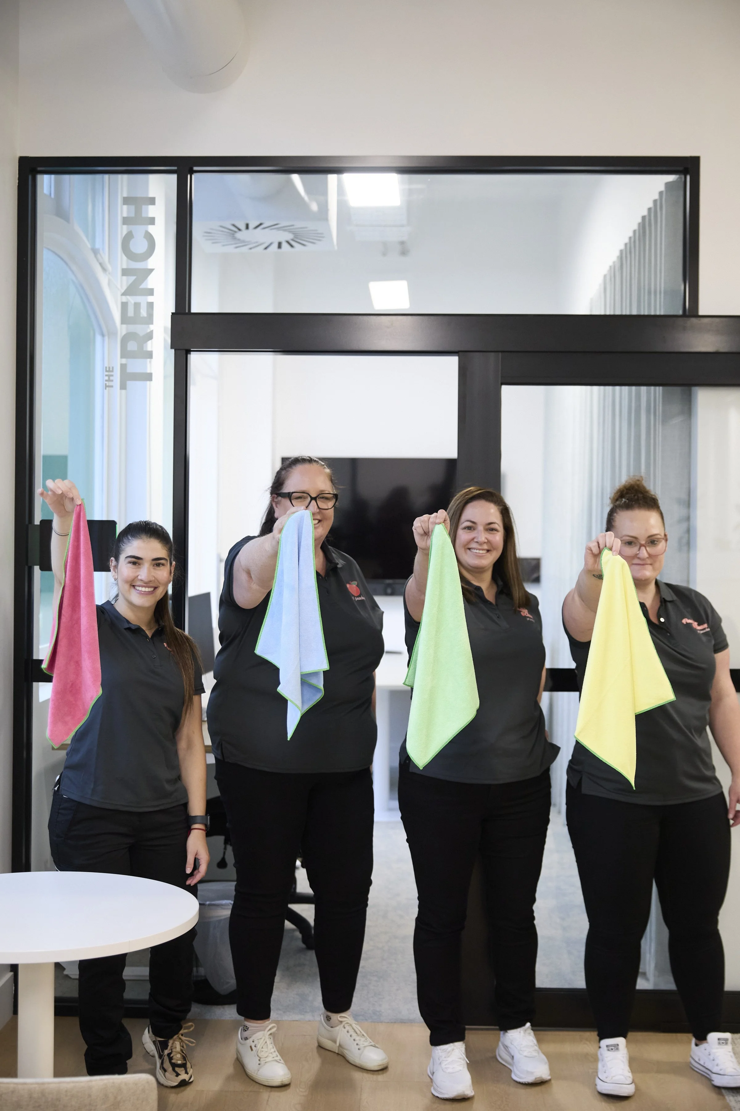 Peachie Clean team holding colour-coded cleaning cloths in modern Hobart office space