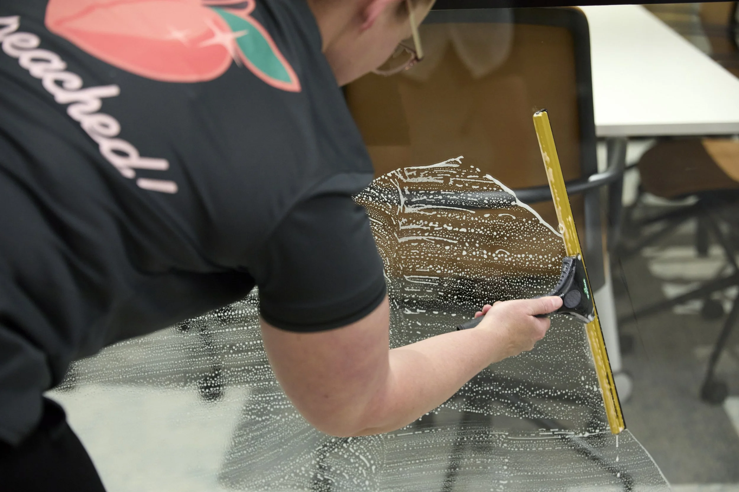 Peachie Clean team member using squeegee to clean glass office partition in Hobart workplace