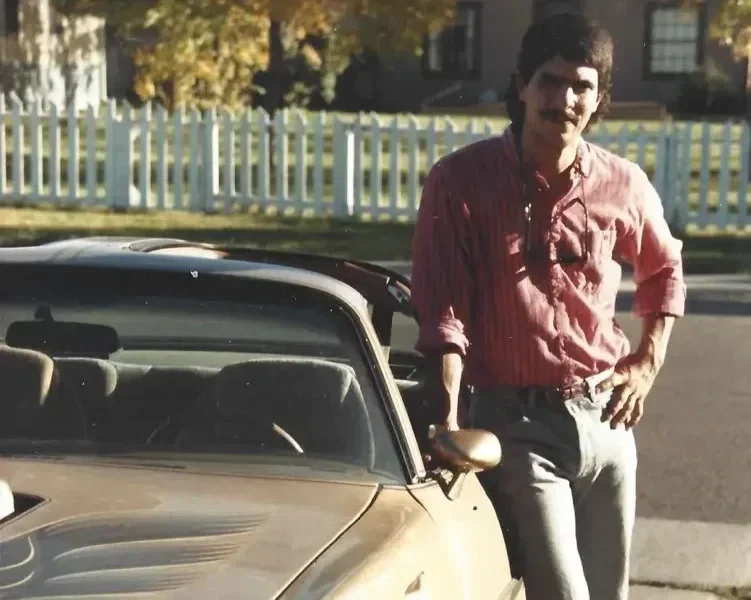 A vintage gold sports car parked outside, with a person partially visible standing next to the passenger side.