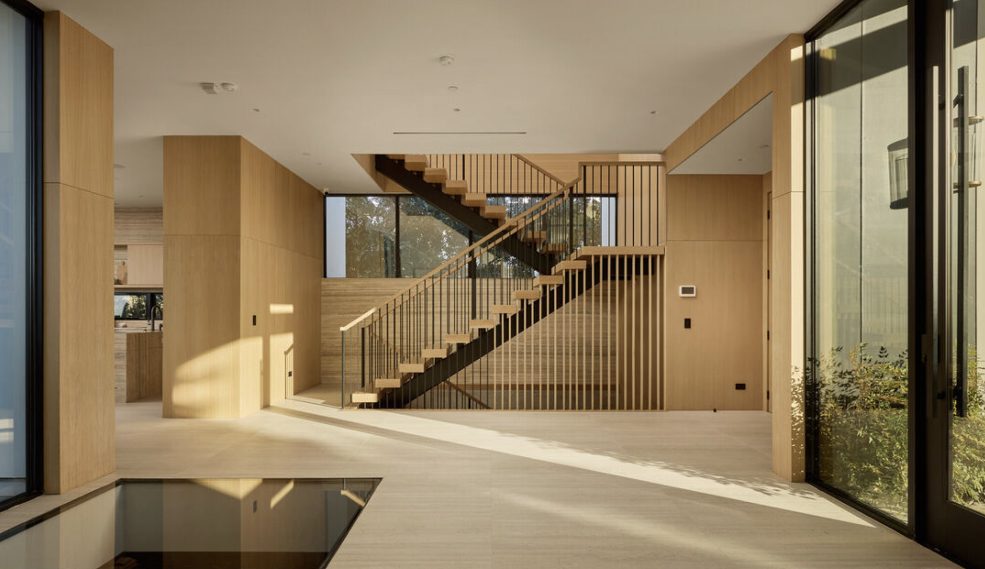 Modern interior with wooden staircase, large windows, and light wood flooring and walls.