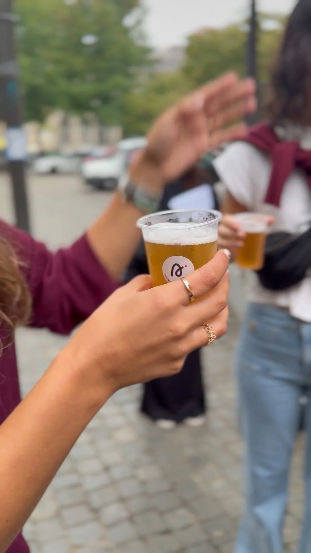 Pessoas segurando um copo de cerveja com autocolantes do SIGNA nos copos, ao ar livre com outras pessoas ao fundo, durante as filmagens de divulgação do SIGNA.