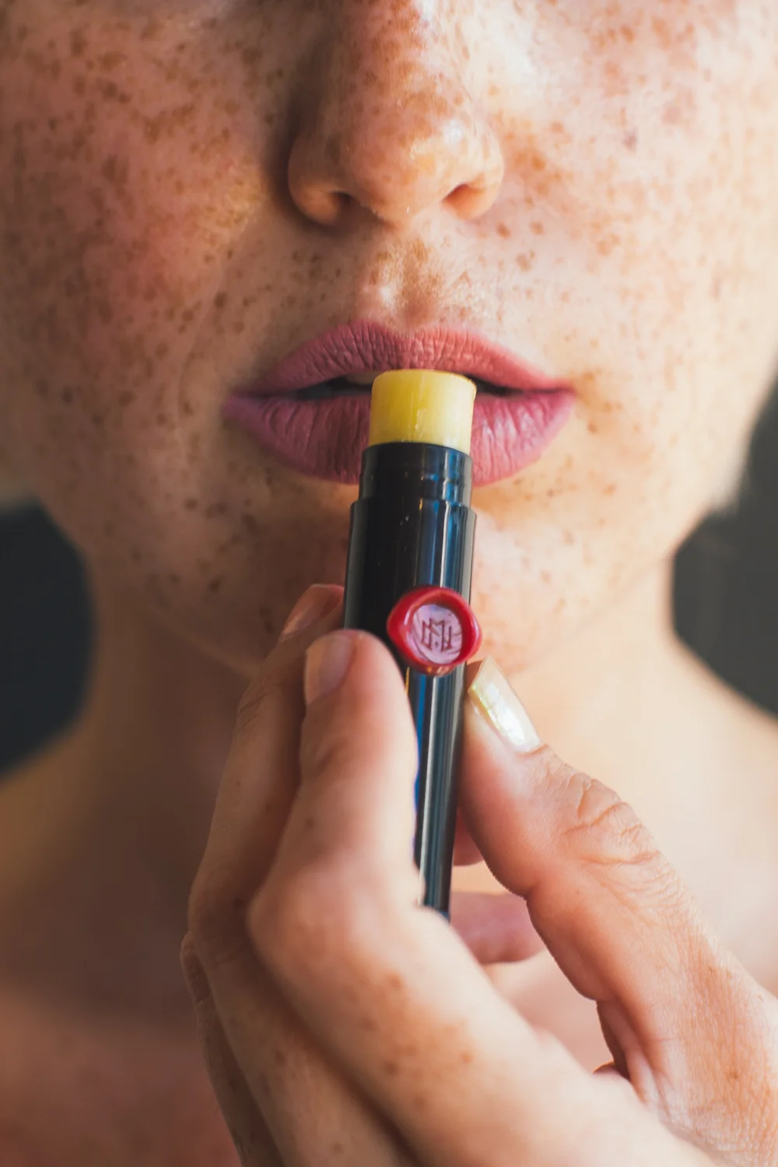 Close-up of a person with freckles applying yellow lipstick.