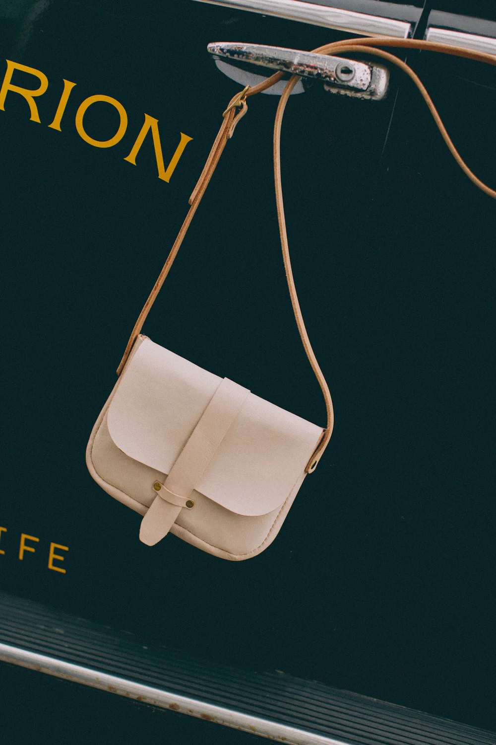 A cream-colored handbag with a strap hanging from a metal hook. The background is dark with yellow letters, part of the word 'FRICTION' visible.