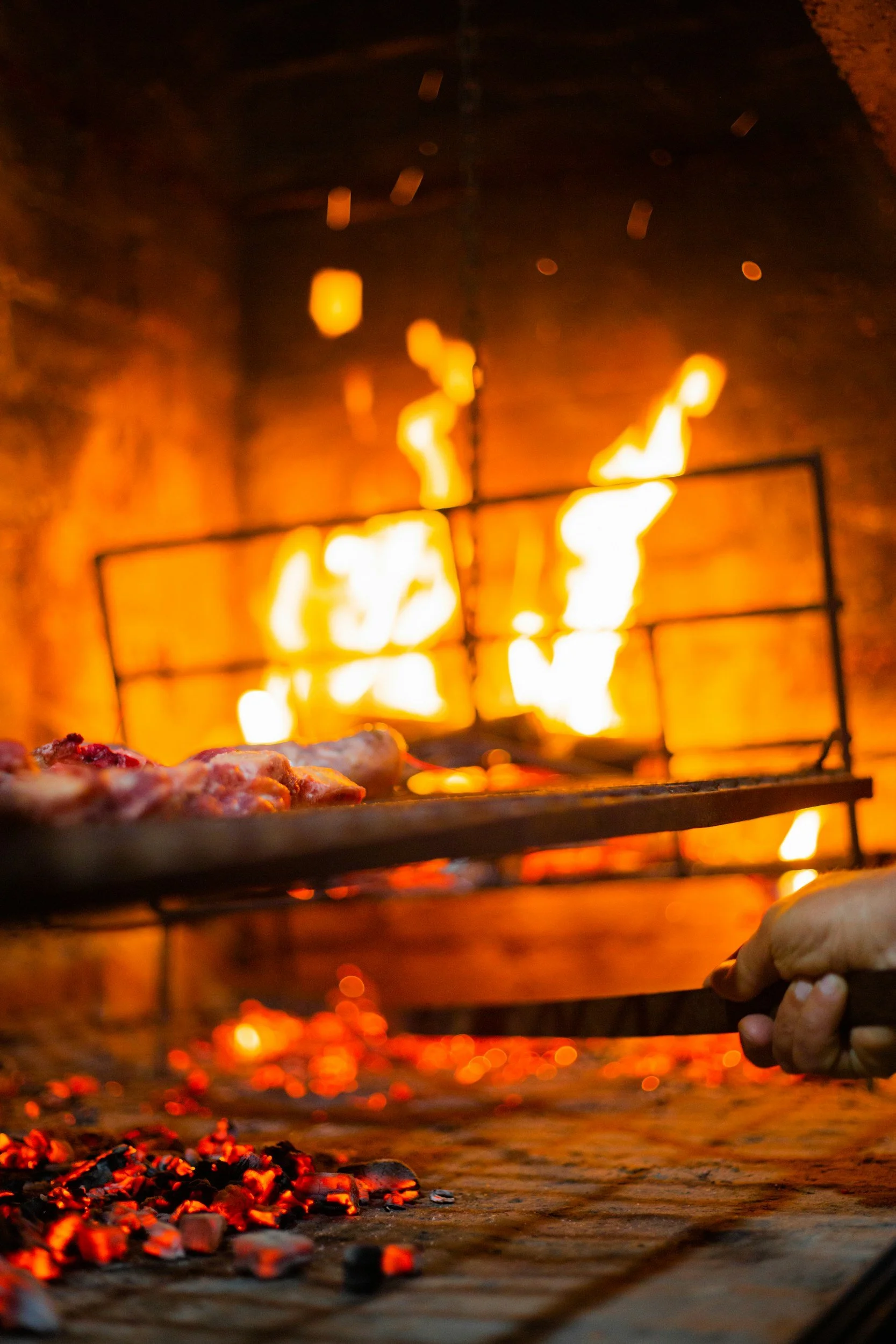 Pizza baking in a wood-fired oven with glowing flames and red hot coals in the foreground.
