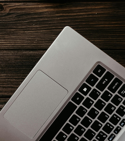 Partial view of a silver laptop keyboard and touchpad on a dark wooden surface.