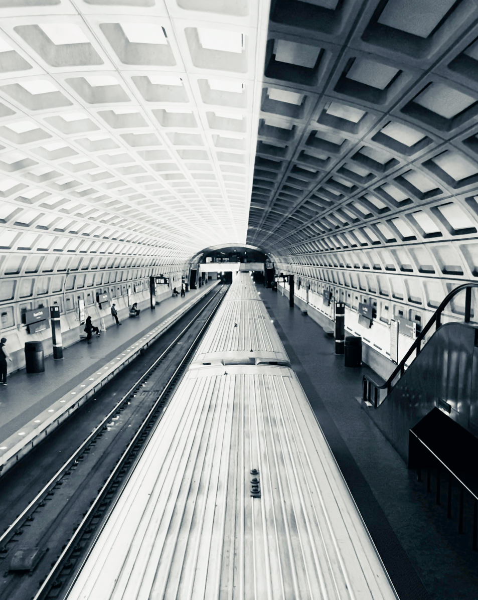 Interior view of a modern subway station with tracks, a platform, and a curved ceiling with geometric patterns.