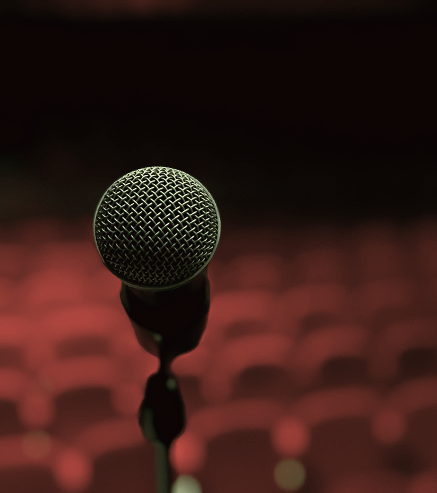 A microphone on a stand in front of an empty auditorium with red seats.