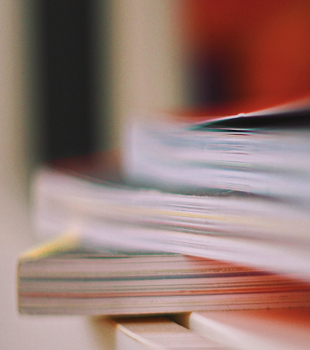 Close-up of stacked books or magazines on a desk or table.