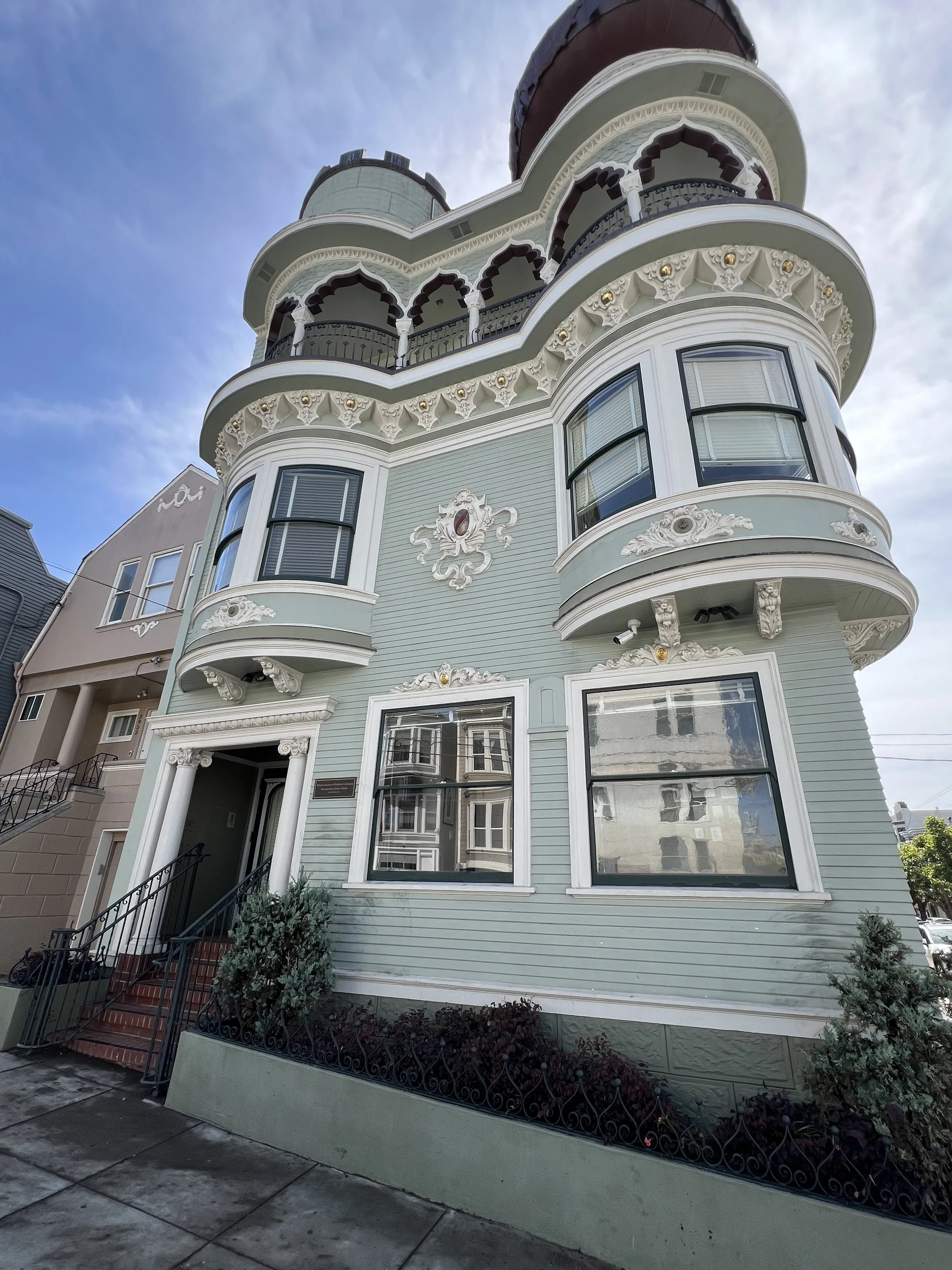 A Victorian-style house with ornate trim, bay windows, and a rounded turret, painted in light pastel colors with decorative architectural details.