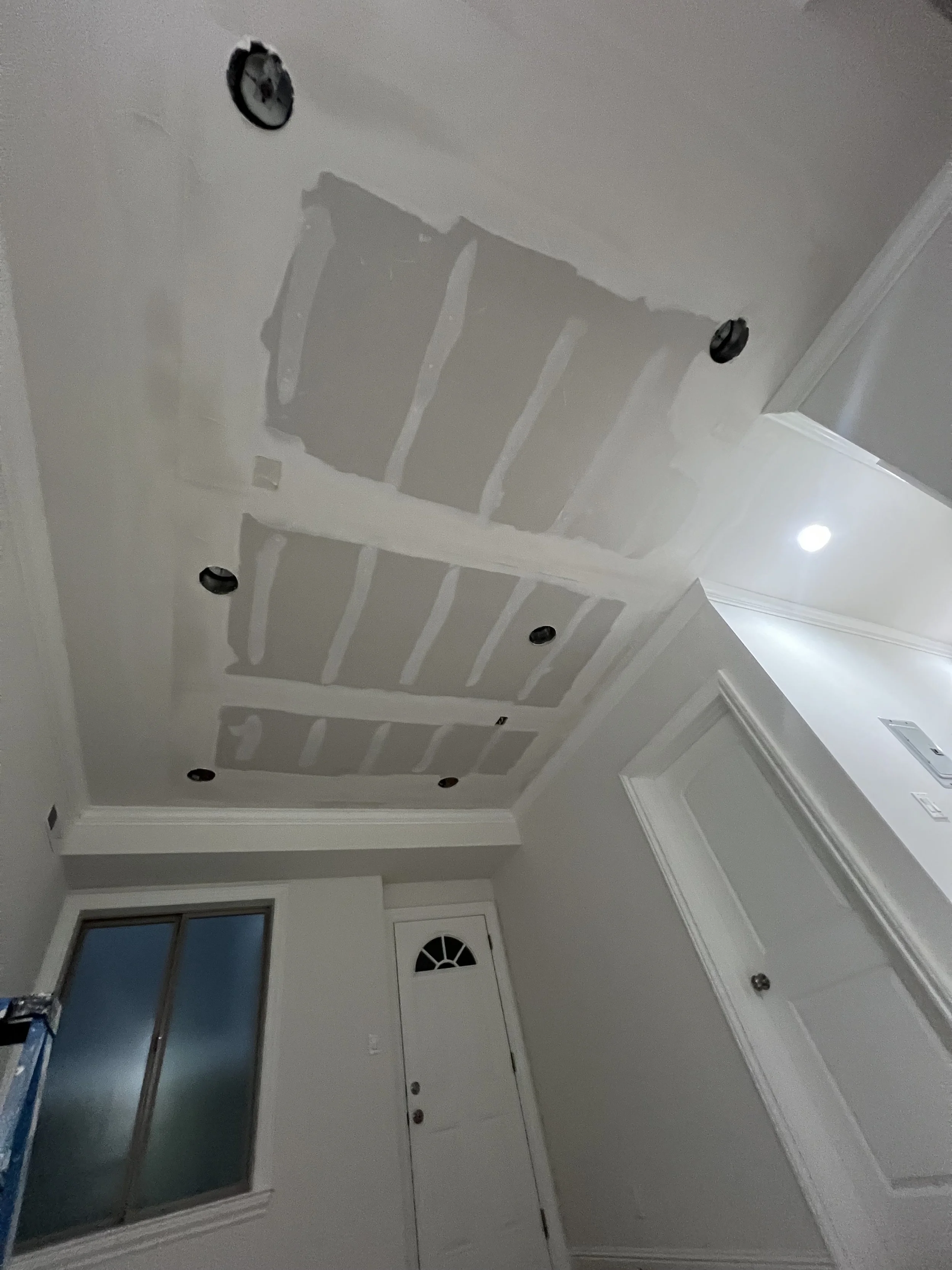 Ceiling with drywall installation and cutouts for recessed lighting, with some light fixtures already installed, in a room under construction or renovation.