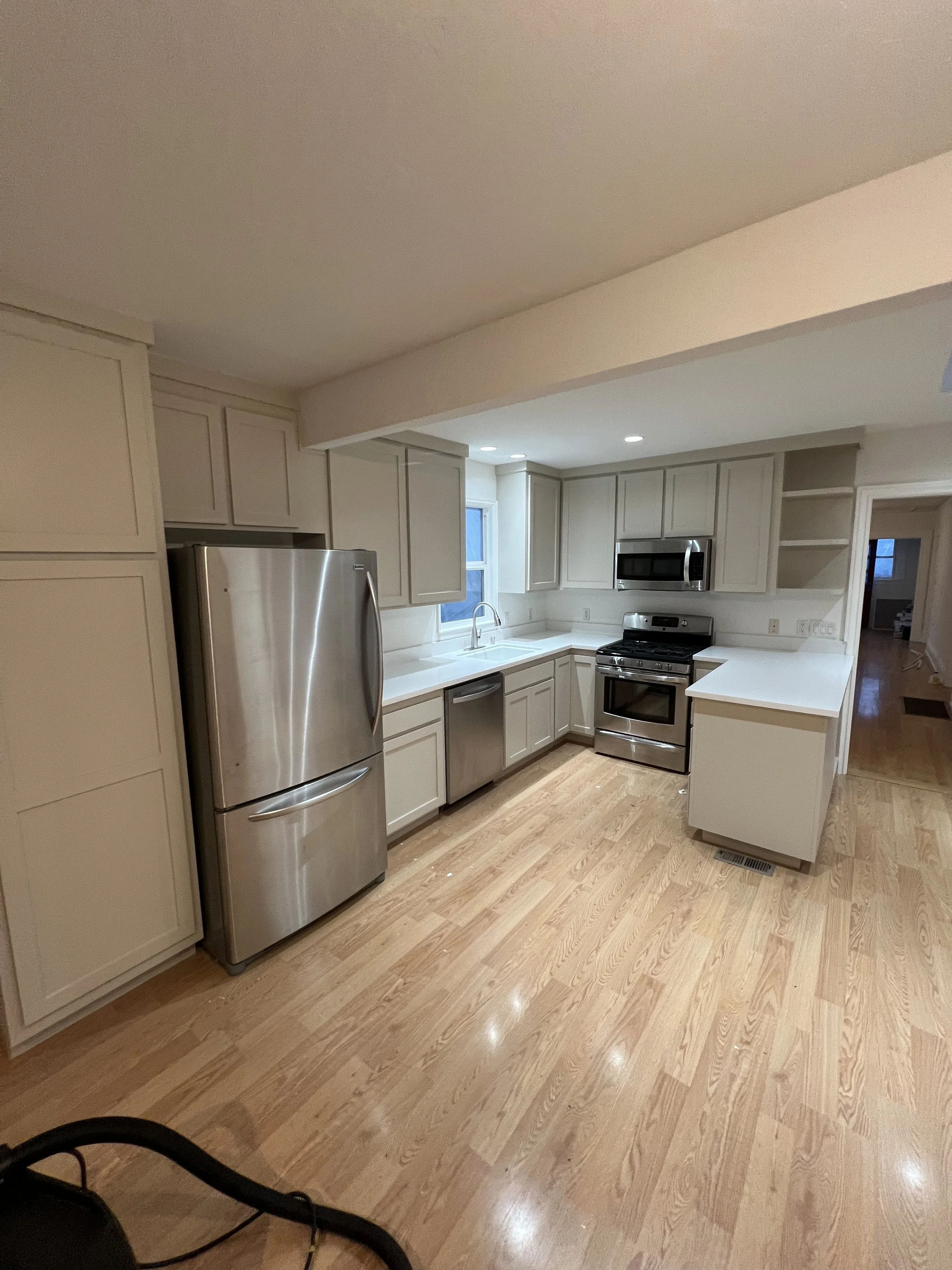 Modern kitchen with light-colored cabinets, stainless steel refrigerator, microwave, and stove, hardwood floors, and a window above the sink.