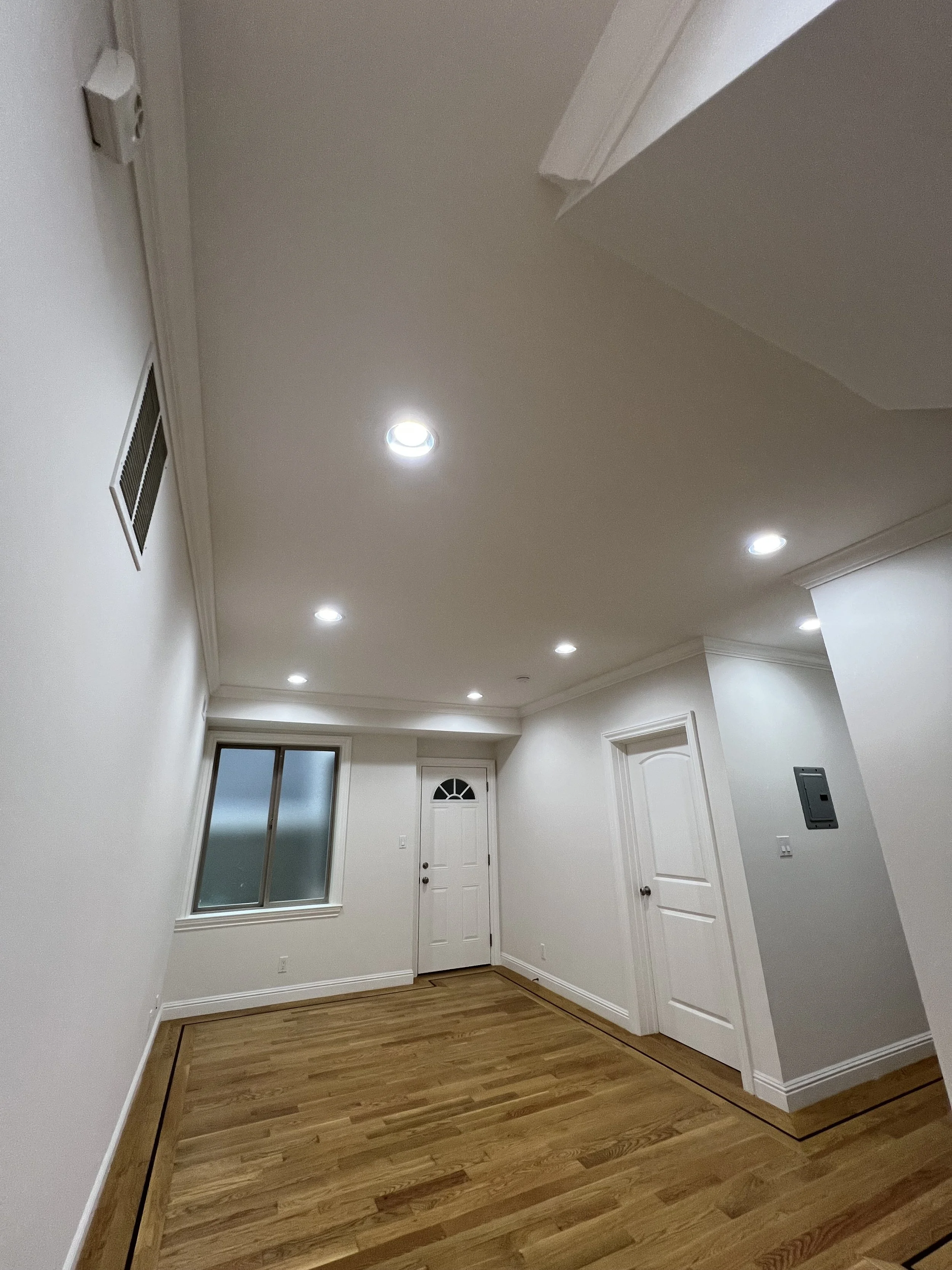 Empty room with white walls, hardwood flooring, multiple ceiling lights, a window with frosted glass, and white doors.