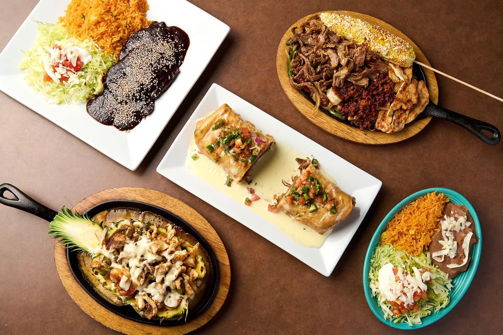 Assorted Mexican dishes including grilled meat, tacos with fillings, sour cream, shredded lettuce, rice, beans, and salad, served on colorful plates and wooden boards.
