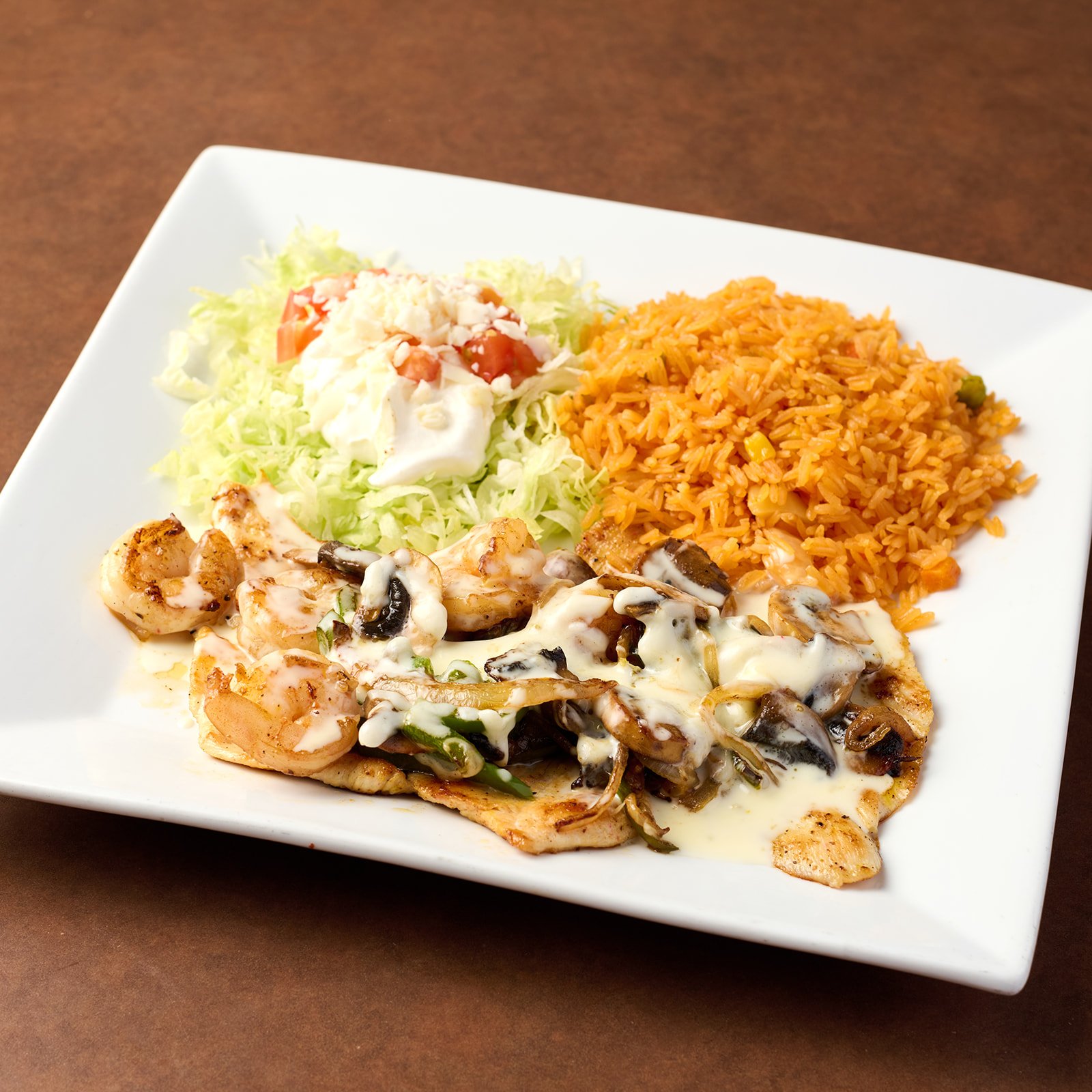 Plate of grilled chicken with mushroom sauce, Mexican rice, and a small salad with lettuce, tomato, and mayonnaise.