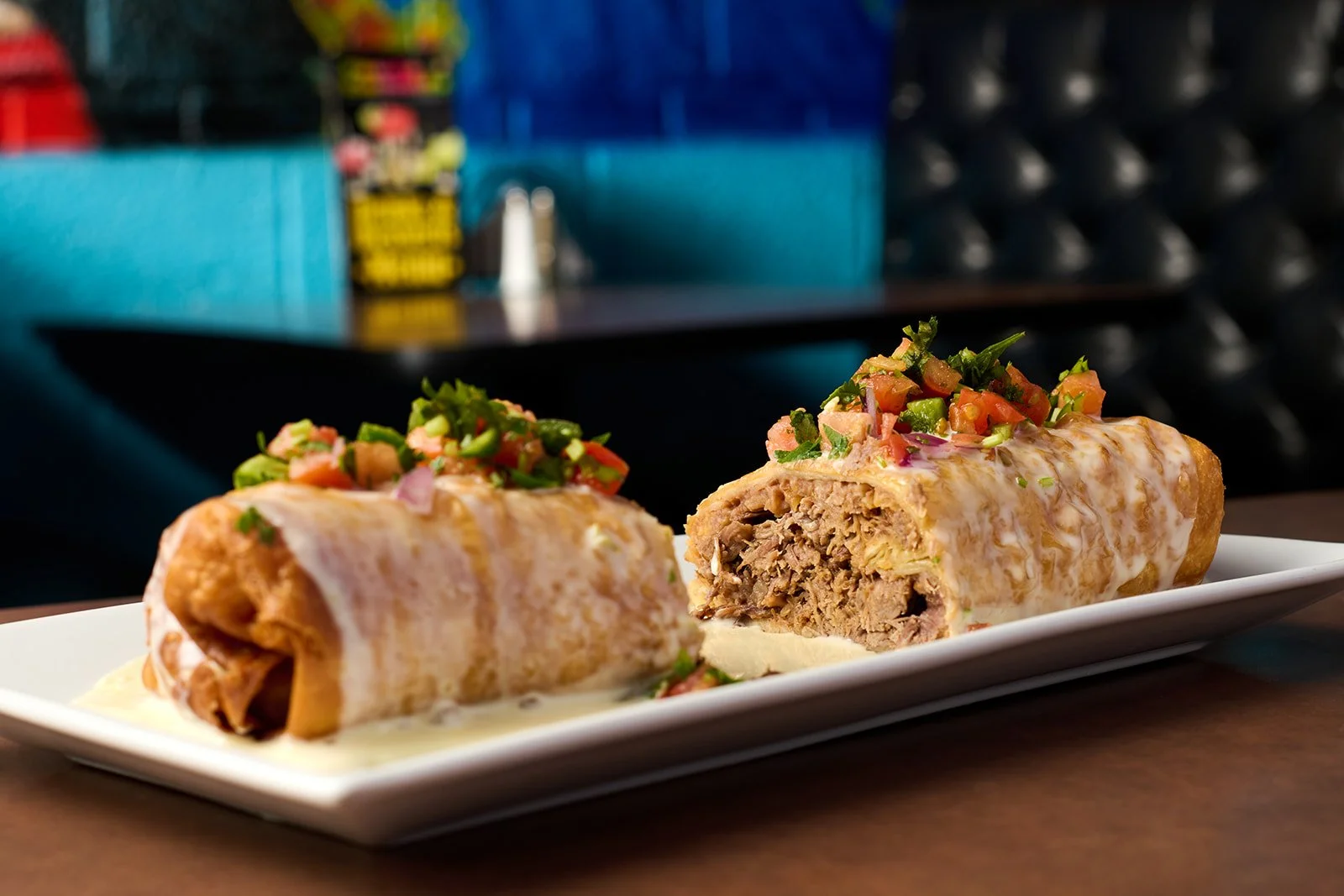 Two Mexican Beef Enchiladas topped with chopped fresh herbs and tomatoes on a white rectangular plate.