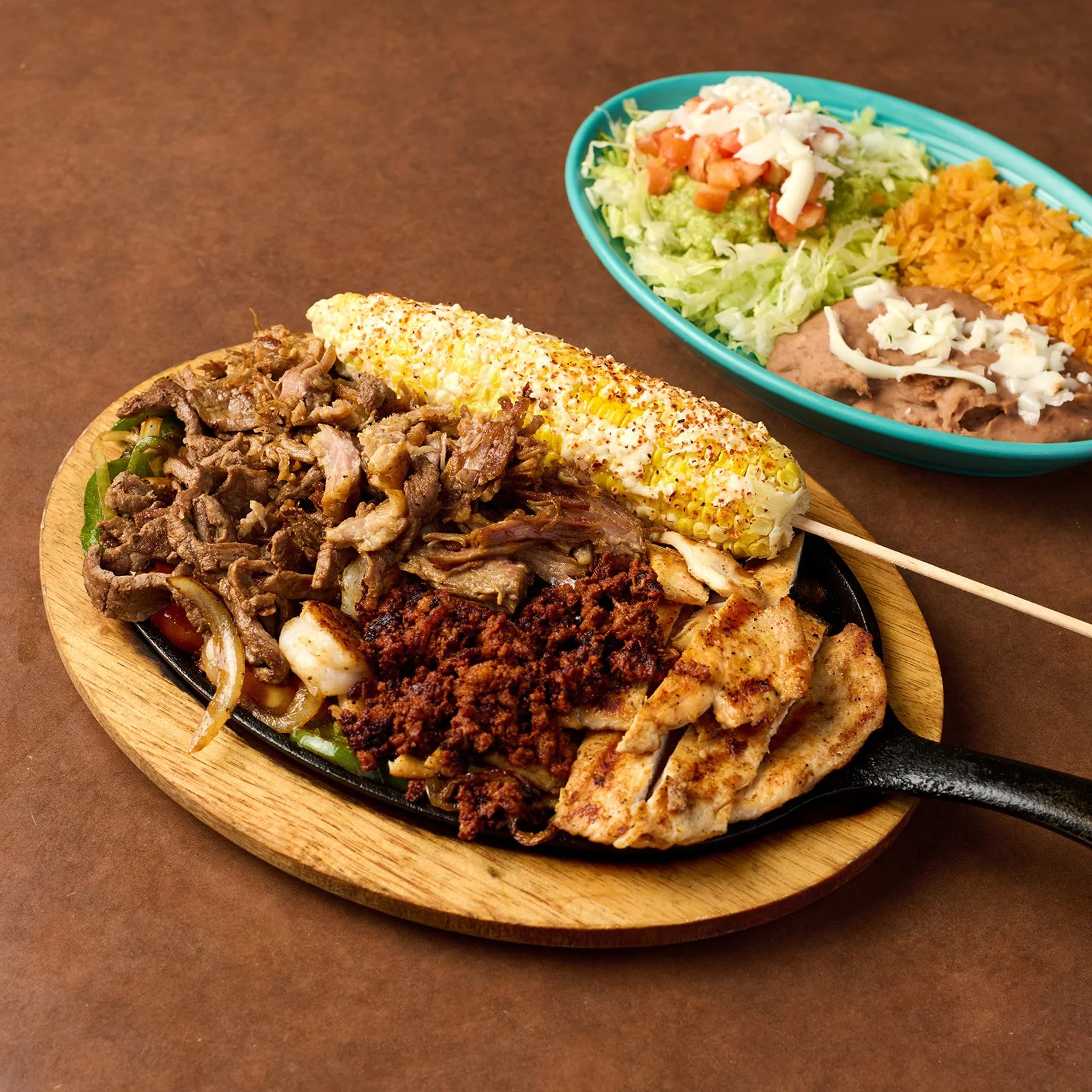 Mexican plate with grilled chicken, beef fajitas, grilled vegetables, and seasoned rice, with a side salad of lettuce, tomato, shredded cheese, and refried beans.