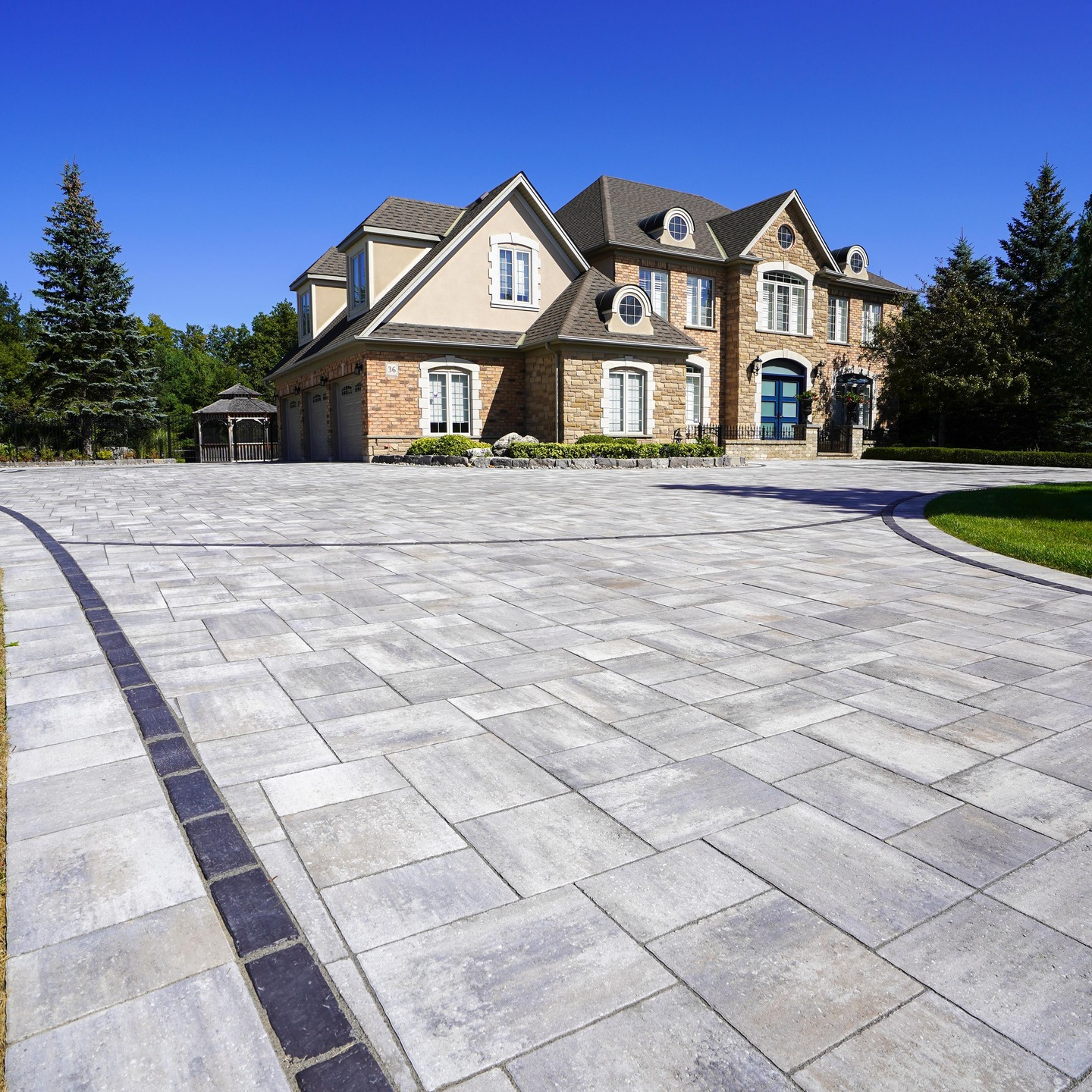 Large house with a stone and stucco exterior, multiple gables, and a spacious paved driveway.