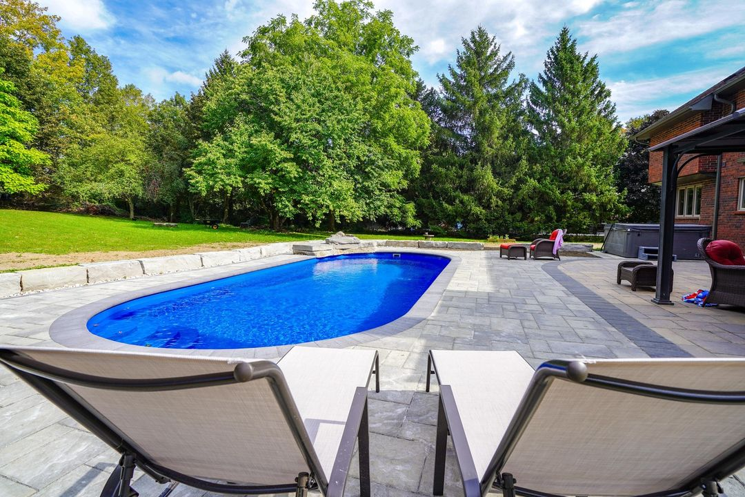 Backyard with a blue swimming pool, two lounge chairs in the foreground, and trees in the background.