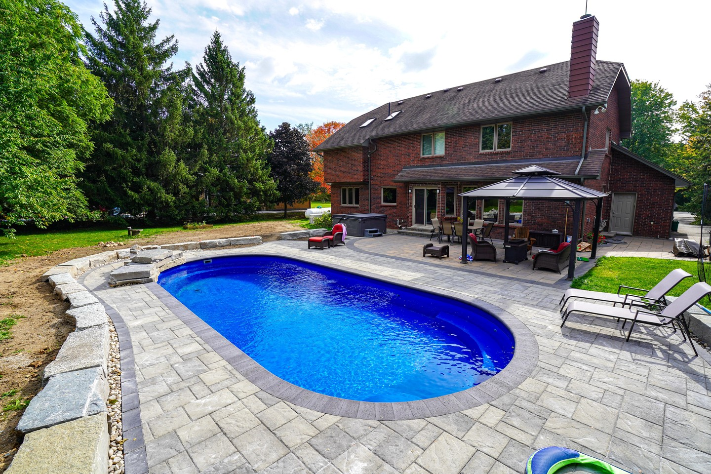 Backyard with a swimming pool, outdoor furniture, and a brick house with a patio and trees around.