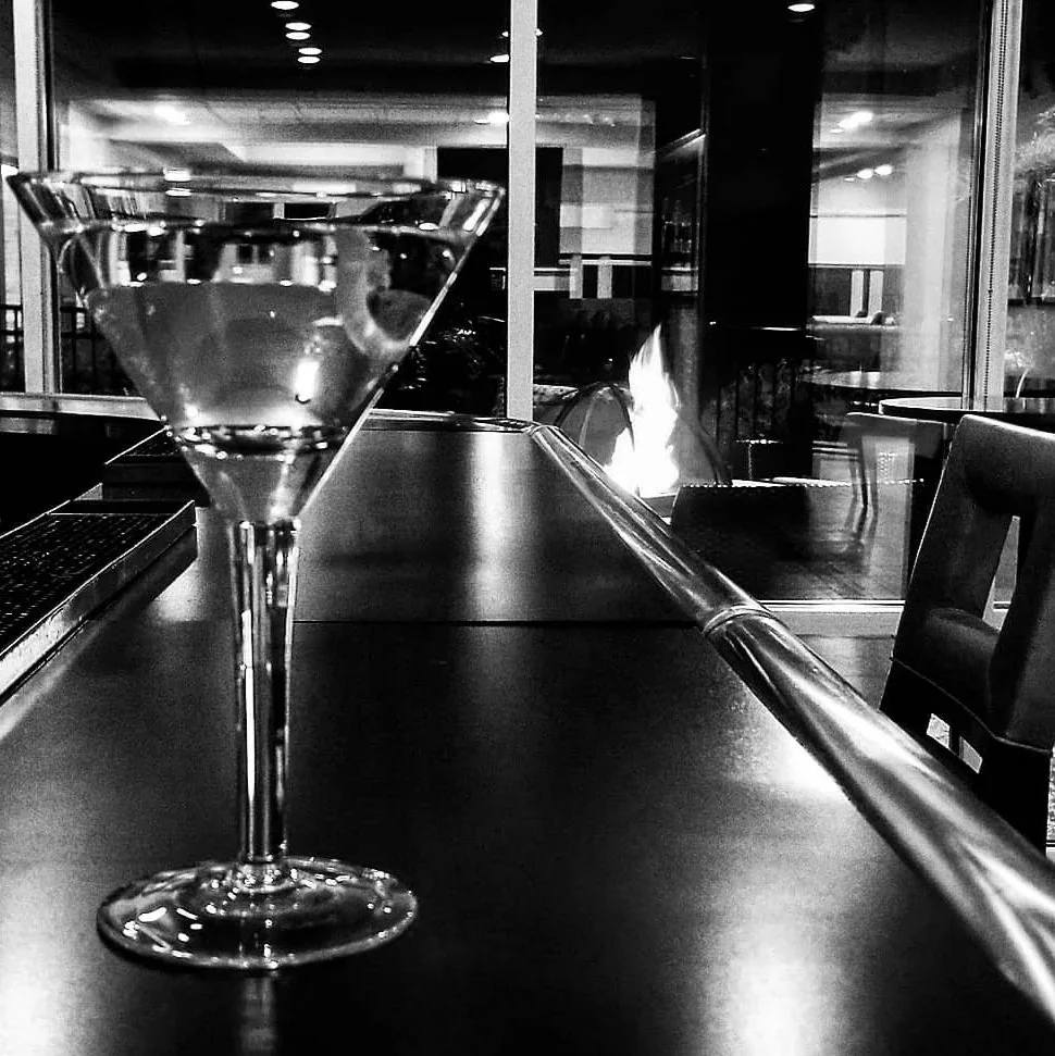 A martini glass on a countertop in a modern indoor setting with a fireplace visible in the background.