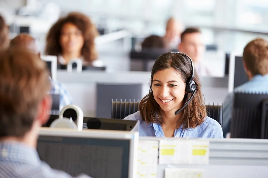 A woman working in a call center wearing a headset and smiling.